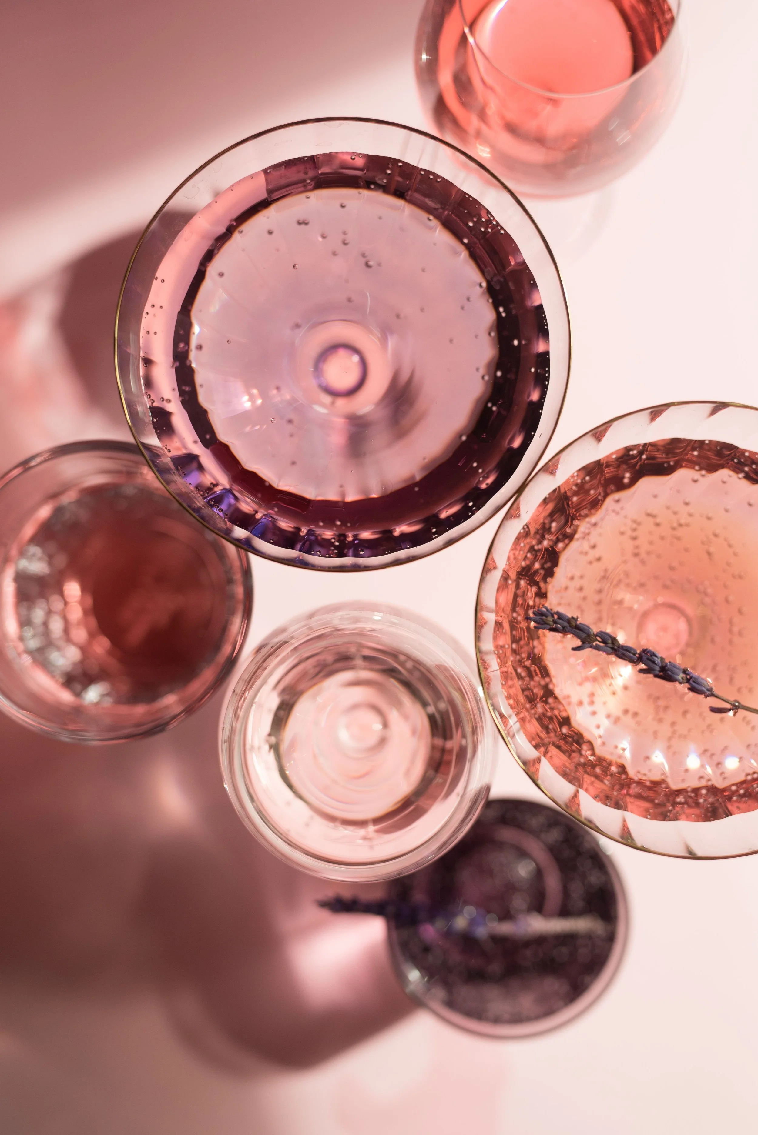 Verres à vin rose disposés sur une surface blanche, certains contenant du vin rosé, vue du dessus.
