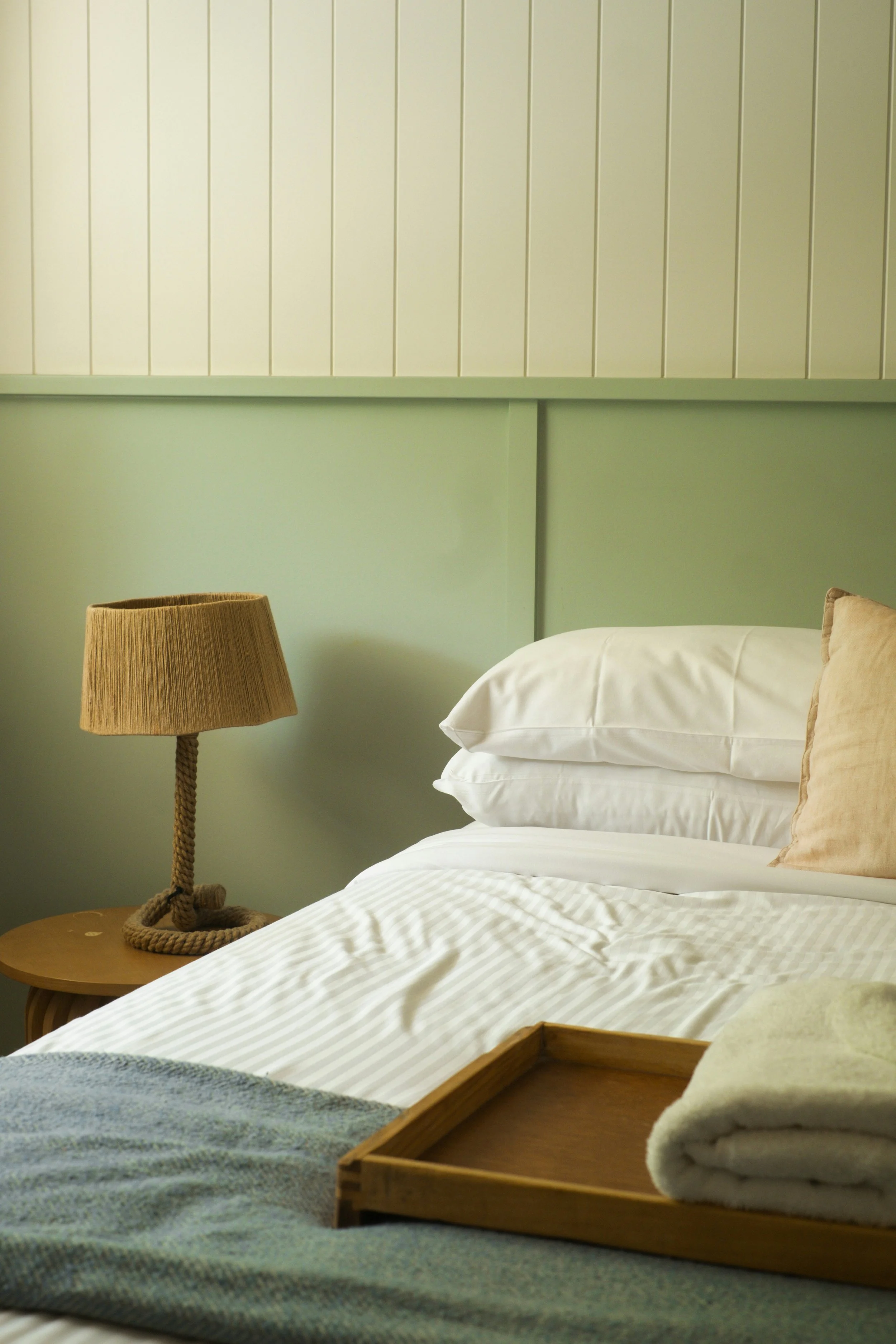 Lits dans une chambre avec une table de chevet et une lampe, oreillers, serviettes et plateau en bois