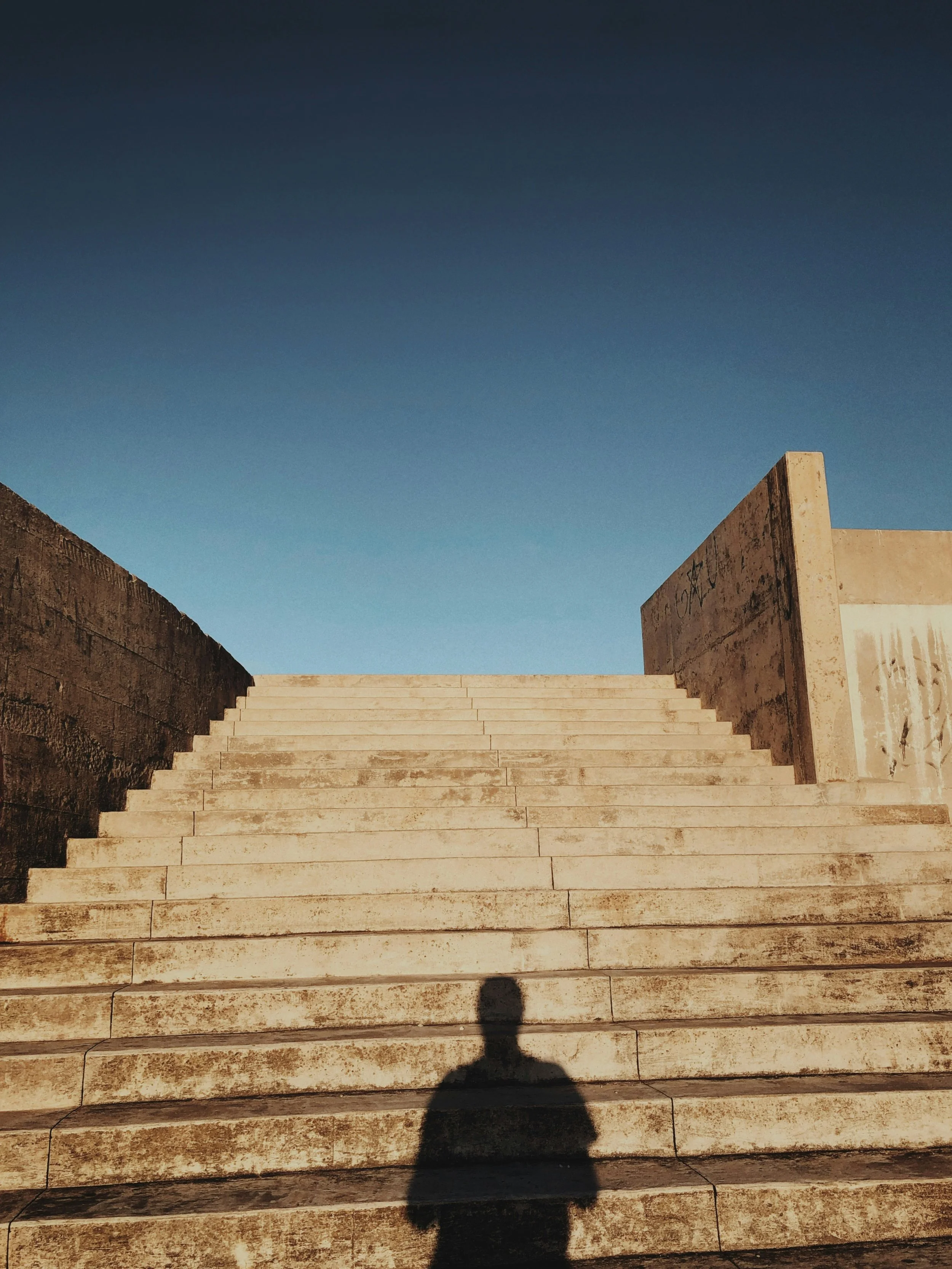 Escaliers en pierre menant vers le ciel avec un ciel bleu clair et une ombre humaine portée sur les marches.
