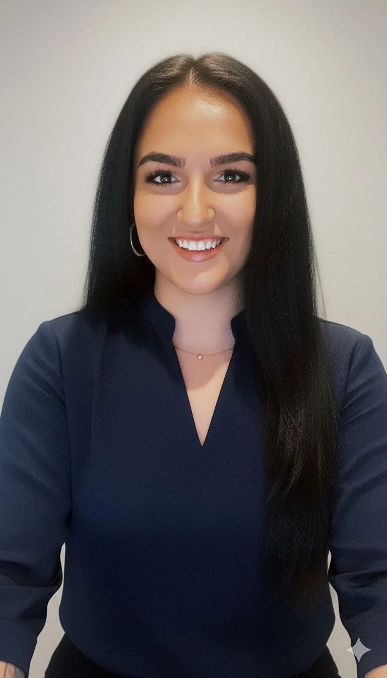 A young woman with long dark hair, wearing a dark blouse and jewelry, smiling at the camera.