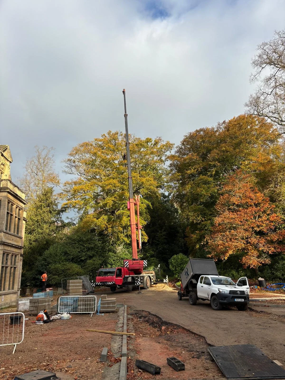 Construction site with a crane, a white pickup truck, and autumn trees in the background.