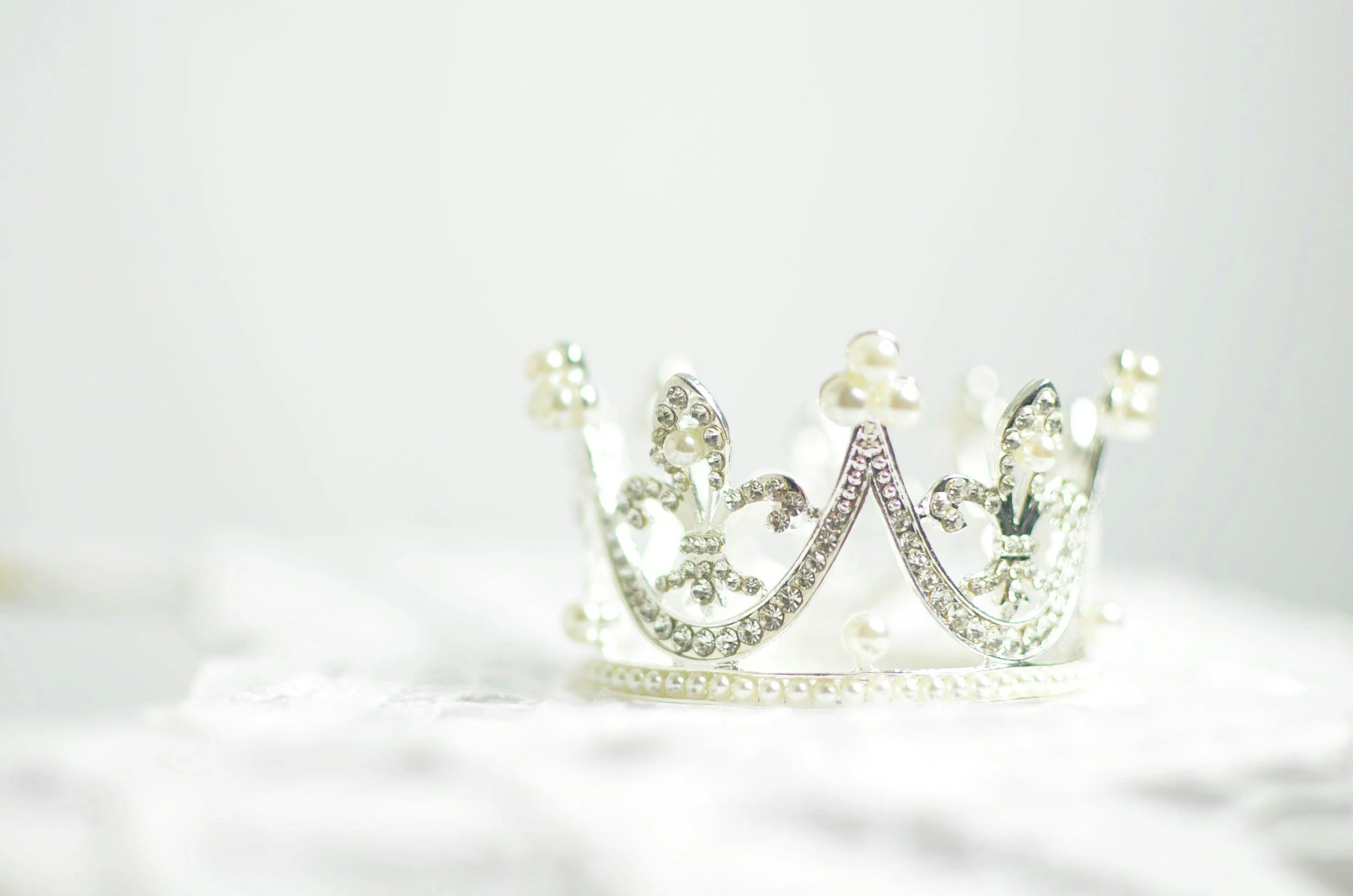 A silver tiara with pearl and rhinestone accents resting on a soft white surface.