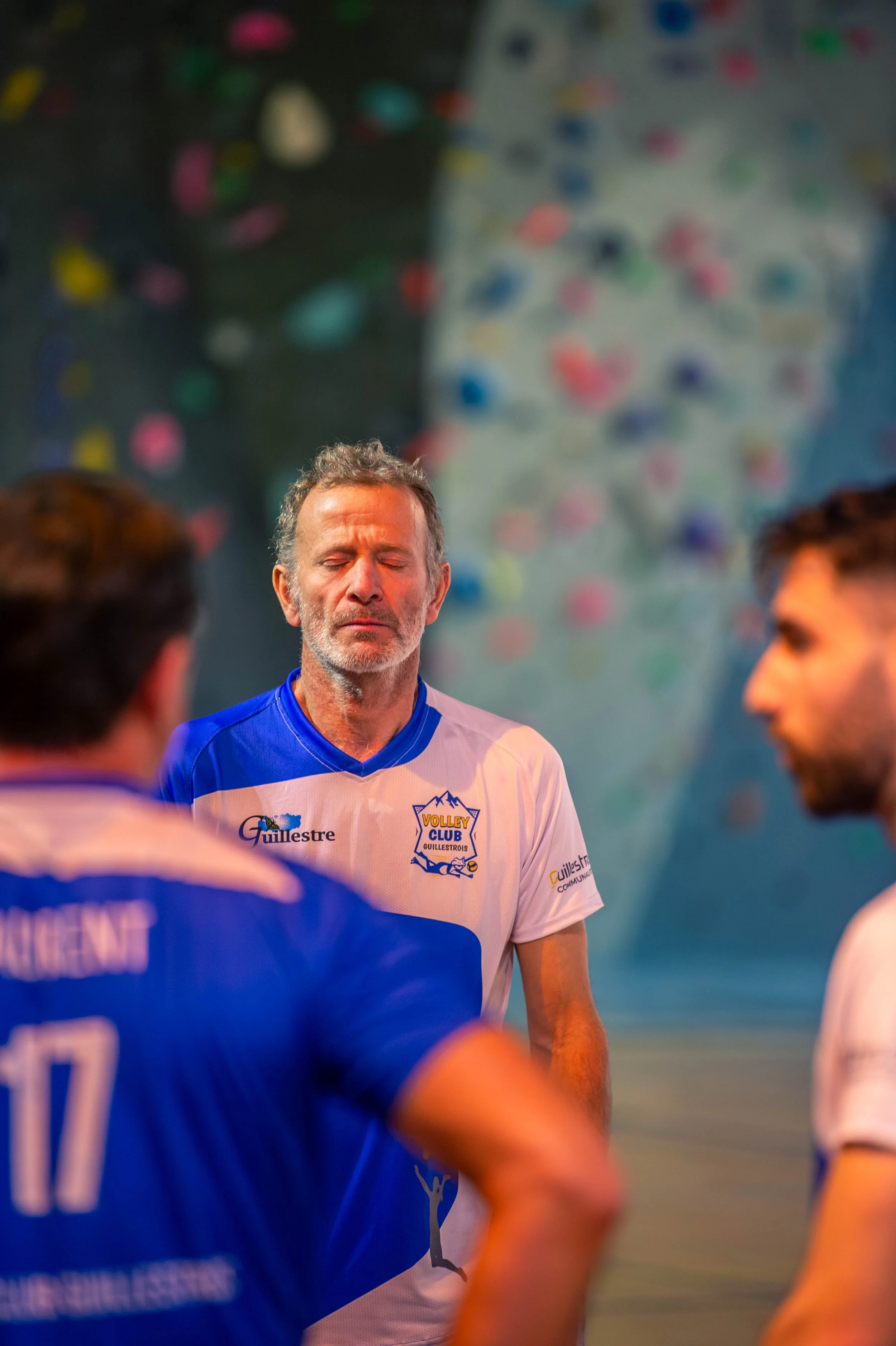Un entraîneur ou un joueur de volleyball en méditation ou en concentration lors d'une pause, avec un mur d'escalade en arrière-plan.