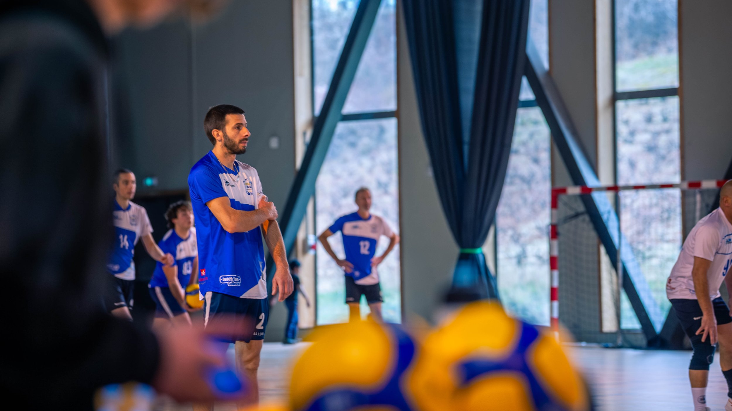Équipe de handball s'entraînant dans une salle intérieure, quelques joueurs portent des maillots bleus et blancs.