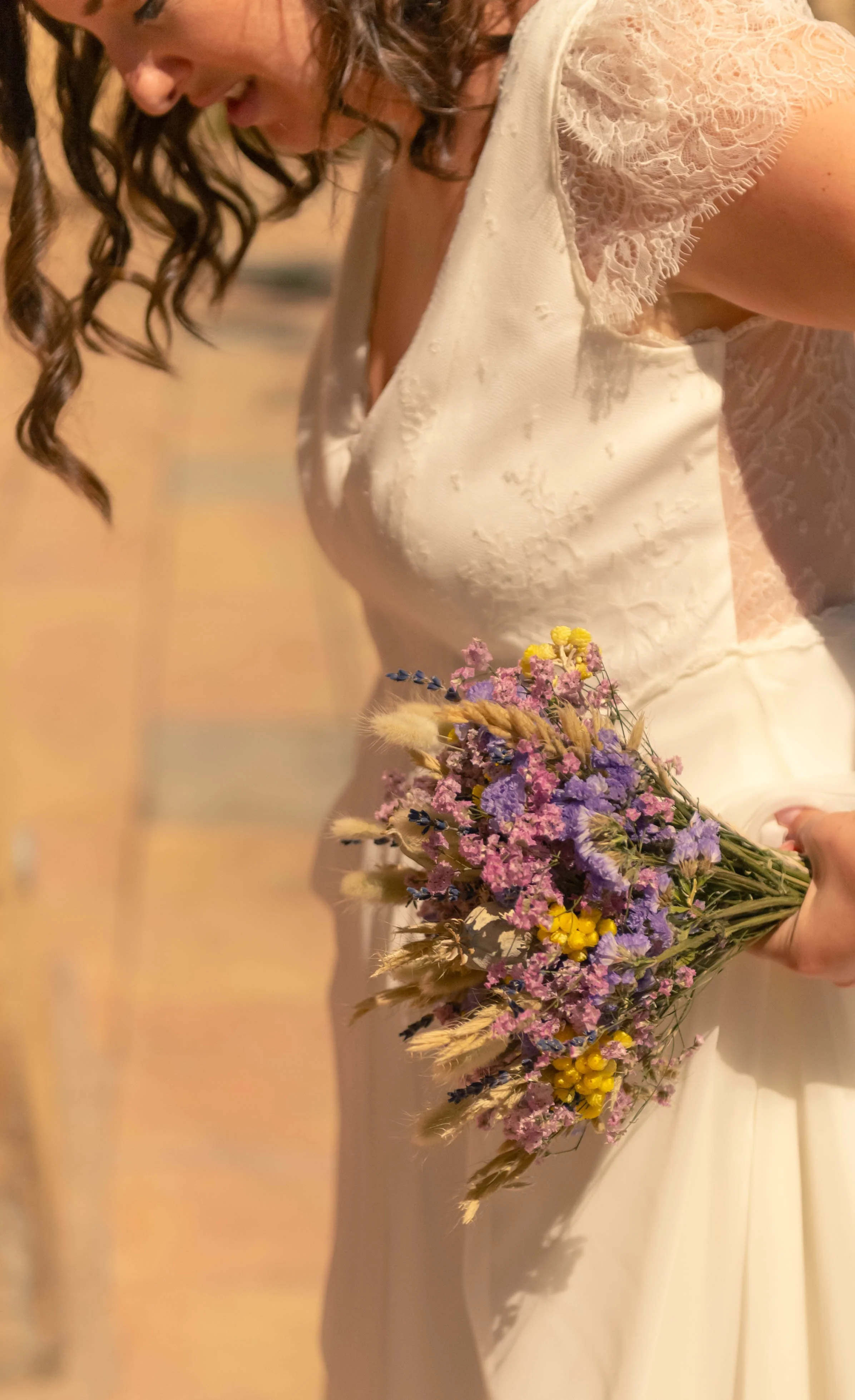 Une femme habillée en robe blanche holding un bouquet de fleurs multicolores, se trouve dans un environnement lumineux.
