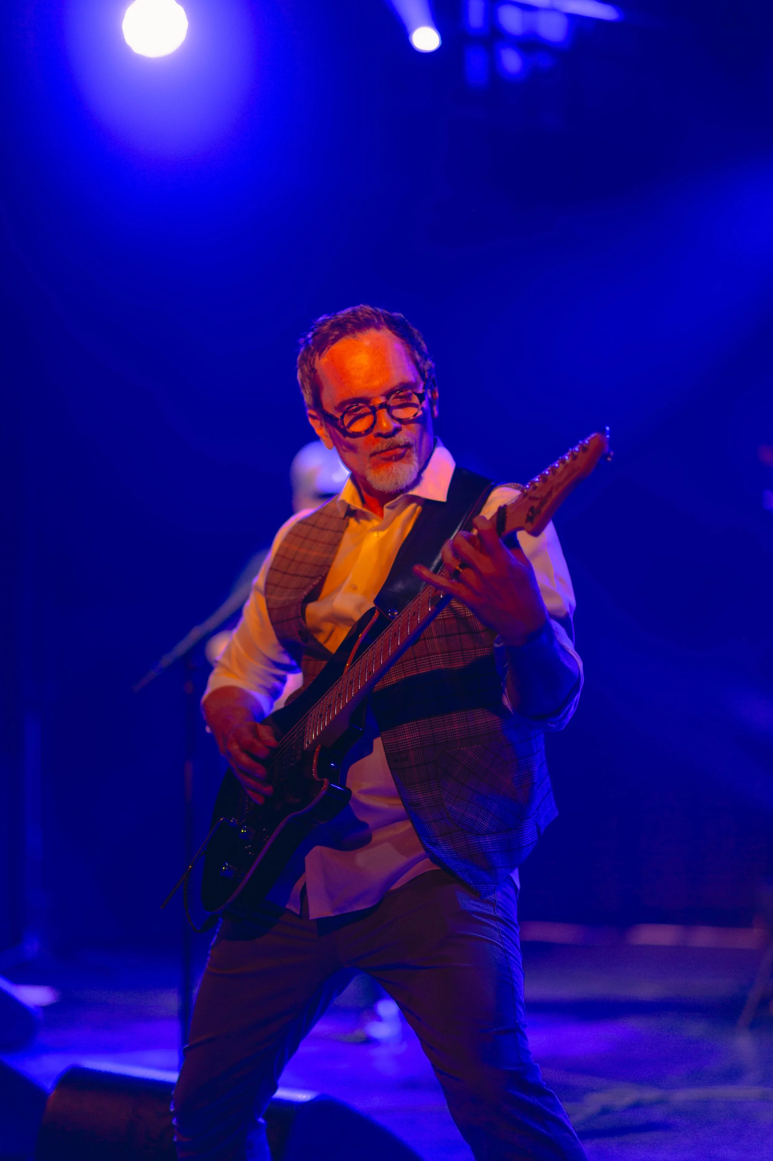 Un homme jouant de la guitare lors d'un concert sous un éclairage violet et bleu.