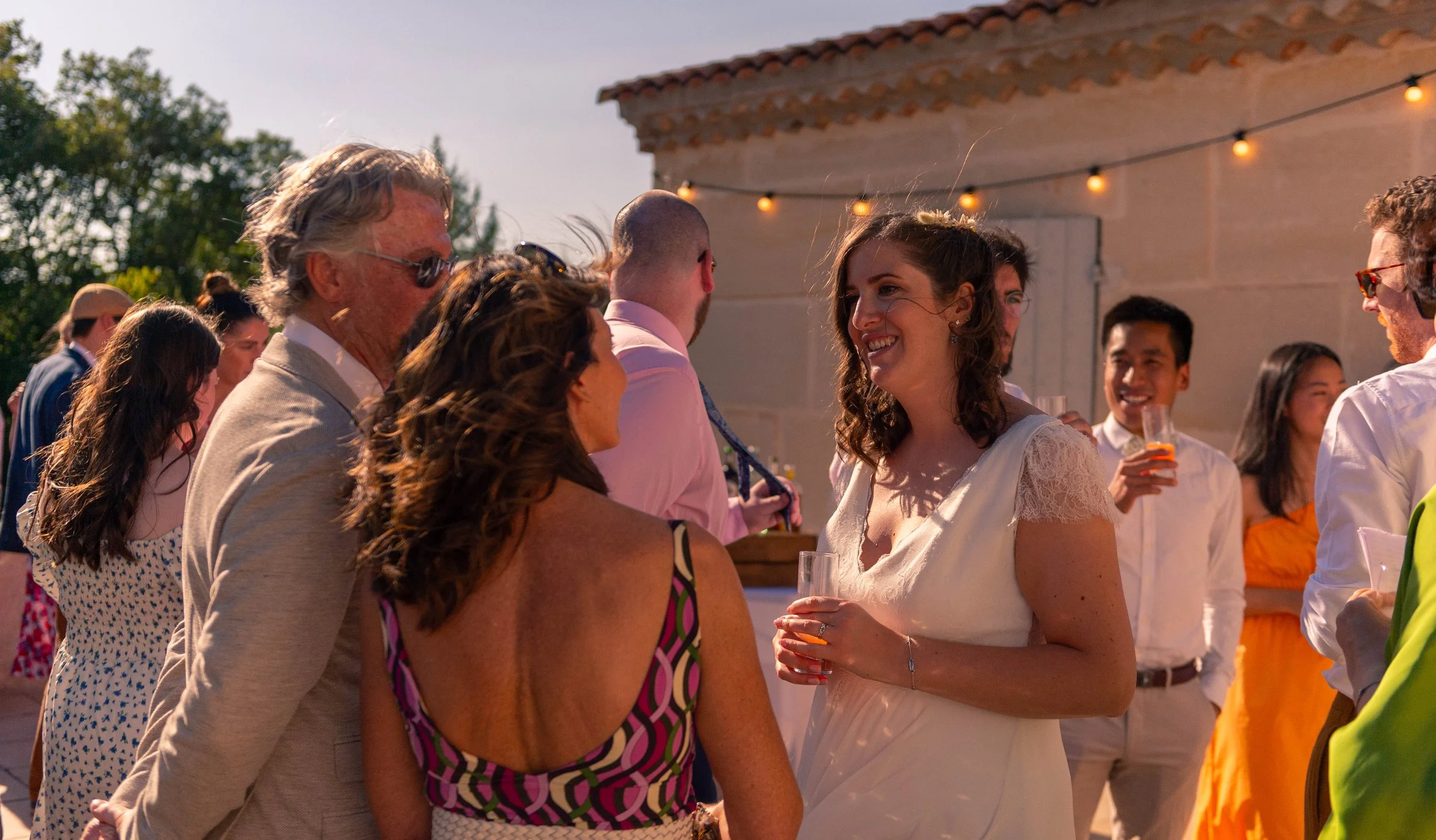 Groupe de personnes célébrant une fête en plein air avec des lumières suspendues, souriant et discutant.