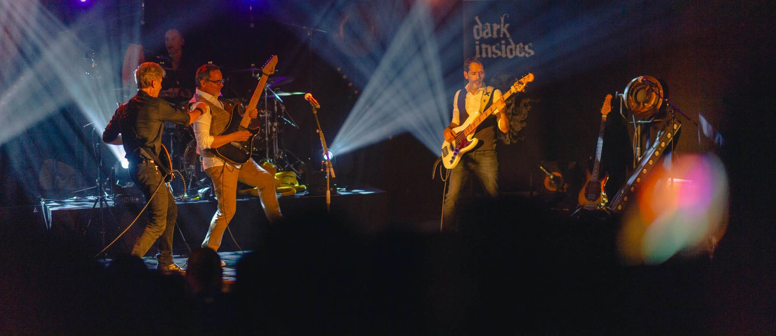 Groupe de quatre musiciens sur scène lors d'un concert, avec lumières colorées et le logo 'dark insides' en arrière-plan.