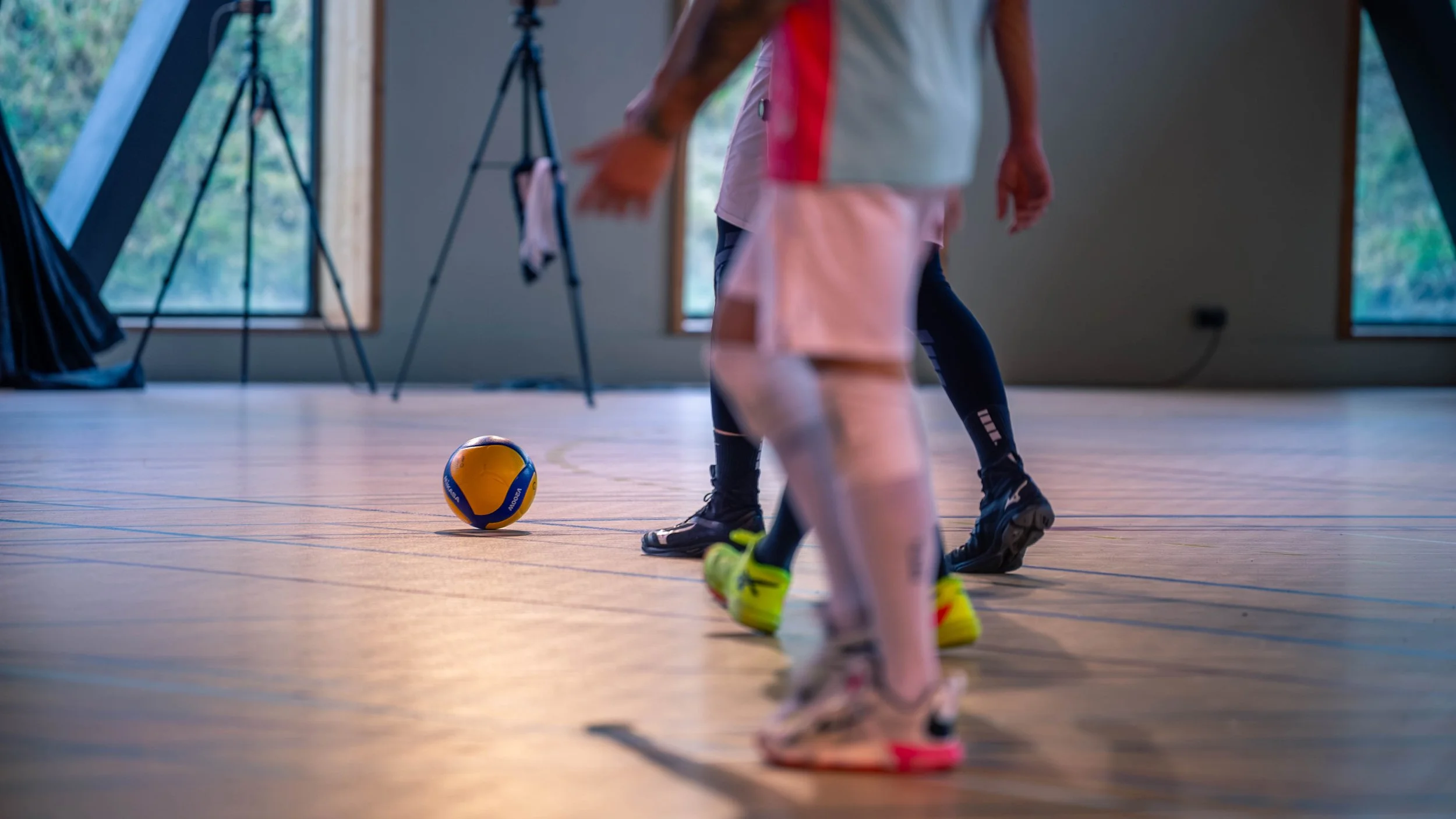 Des enfants jouent au volleyball en intérieur, avec un ballon sur le sol, dans une pièce lumineuse et spacieuse.