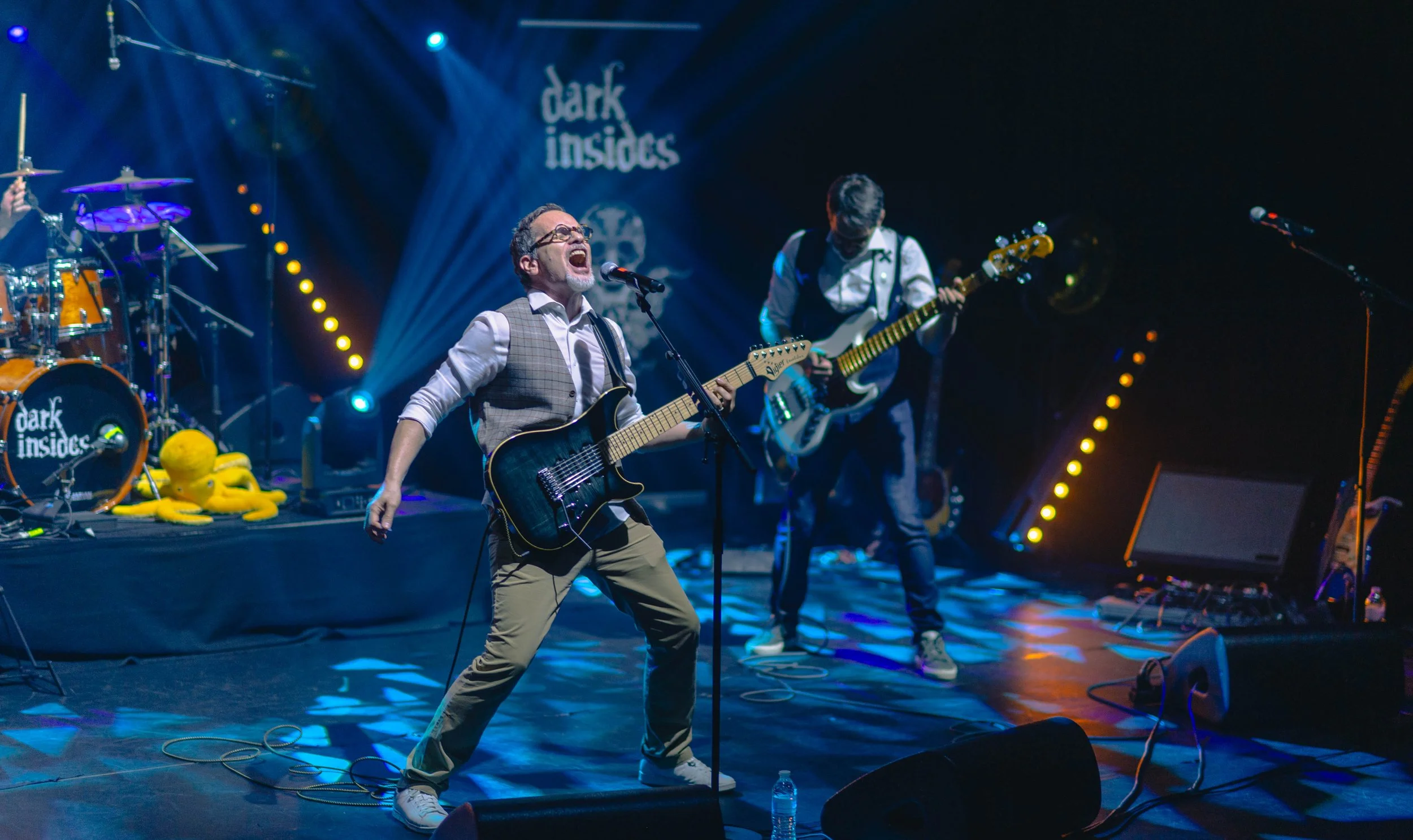 Un groupe de musiciens en performance sur scène avec une lumière dynamique et un logo 'dark insides' en arrière-plan.
