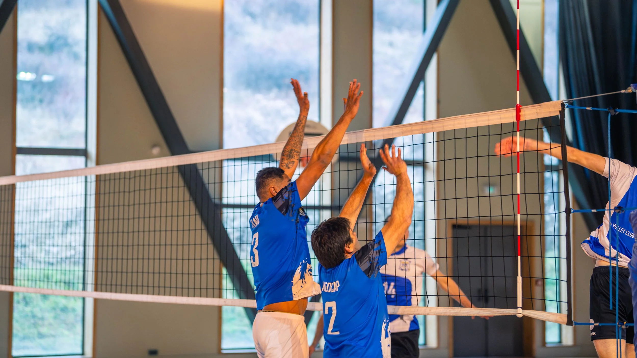 Joueurs de volleyball en action lors d'un match indoor, sautant pour bloquer la balle.