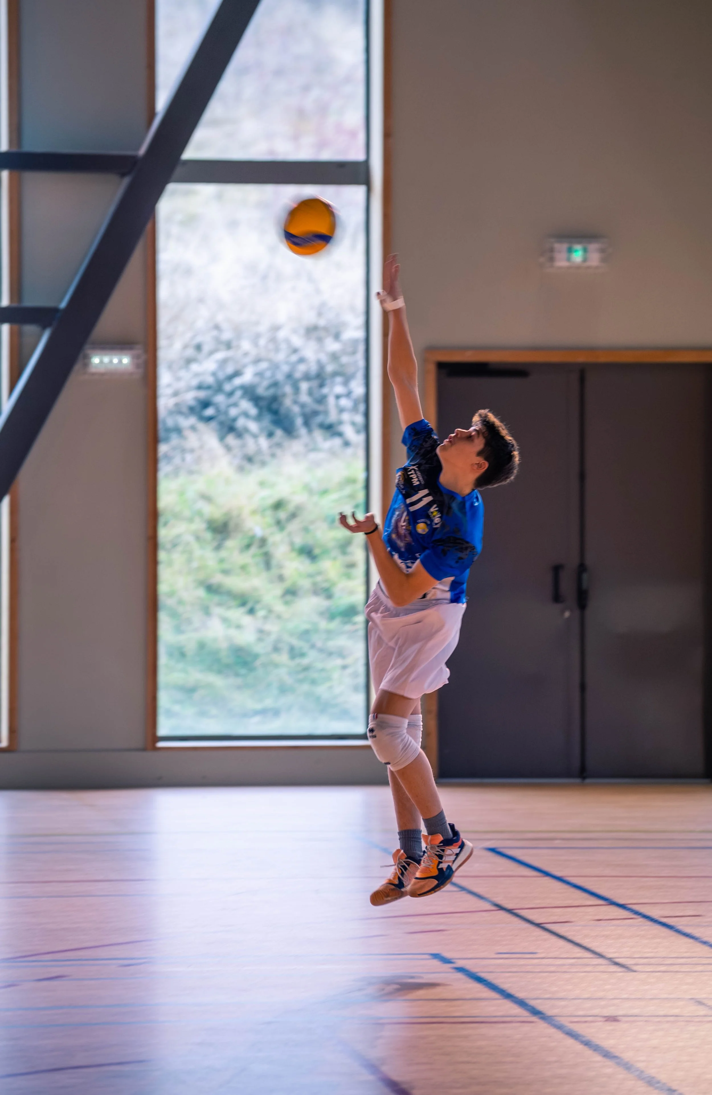 Un jeune garçon joue au volleyball en intérieur, sautant pour frapper le ballon avec le bras levé.