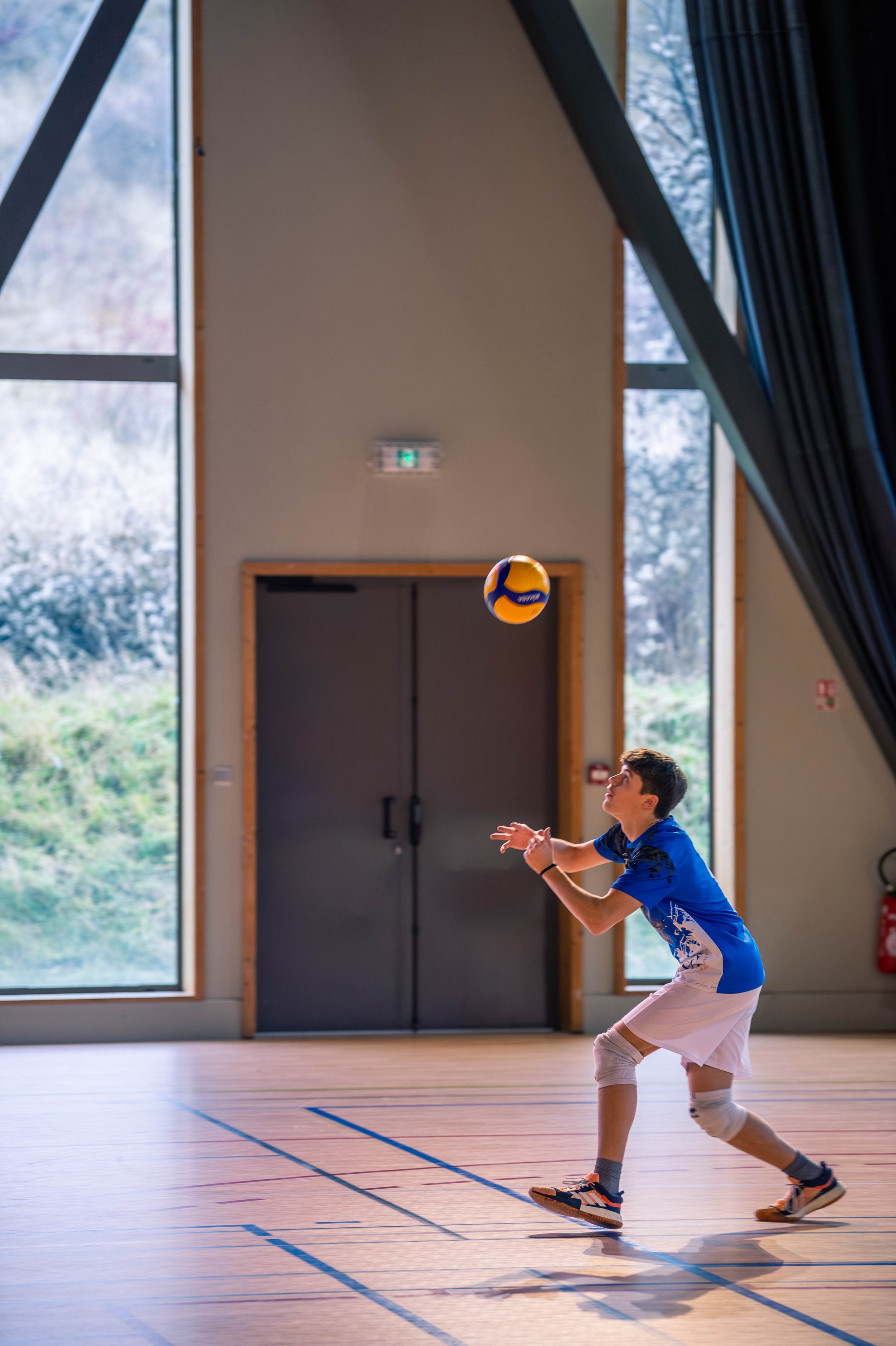 Un garçon jouant au volleyball à l'intérieur d'une salle de sport, prêt à recevoir le ballon.