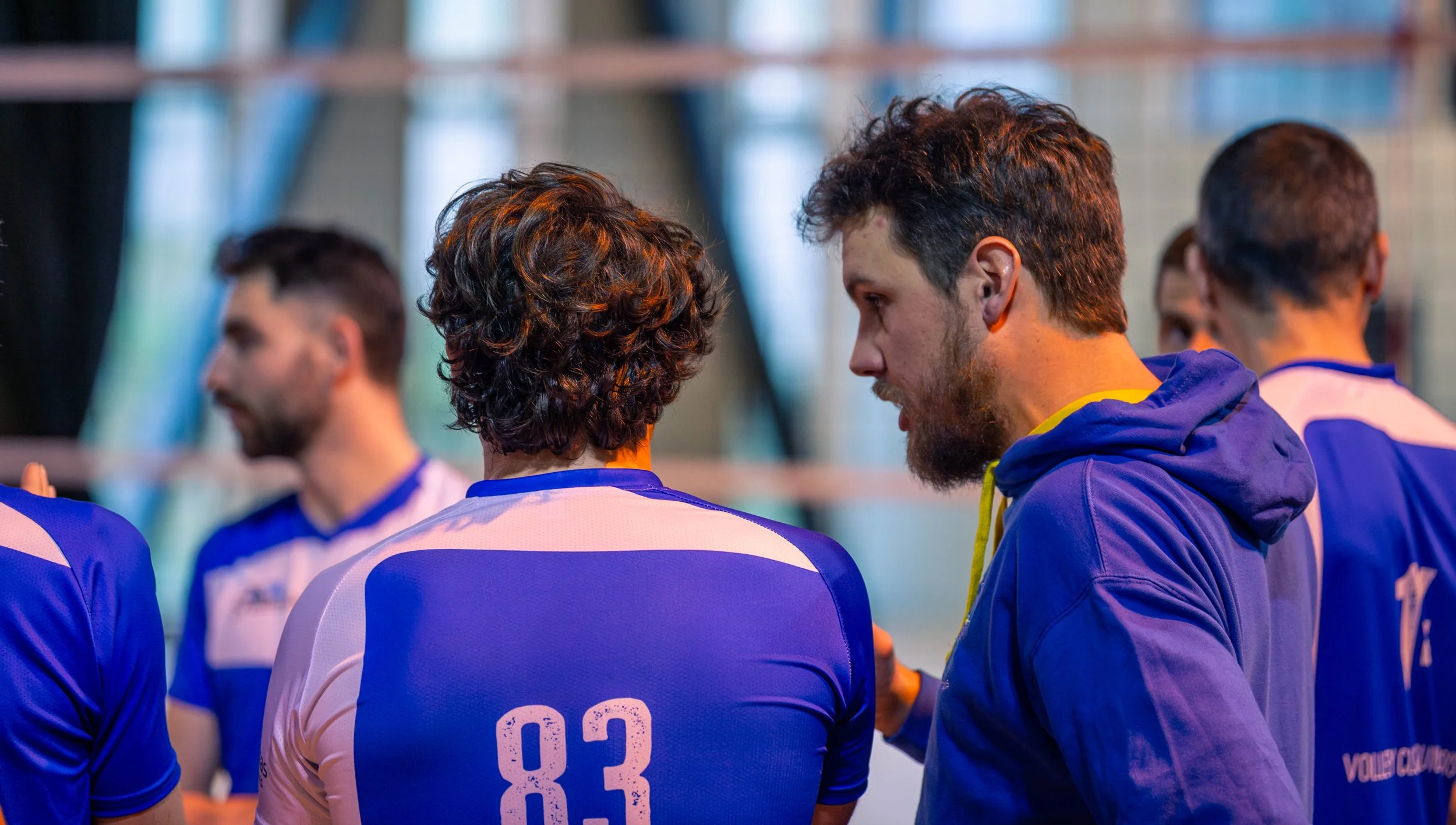 Joueurs de volleyball en tenue bleue, en train de discuter lors d'une rencontre ou entraînement dans un gymnase.
