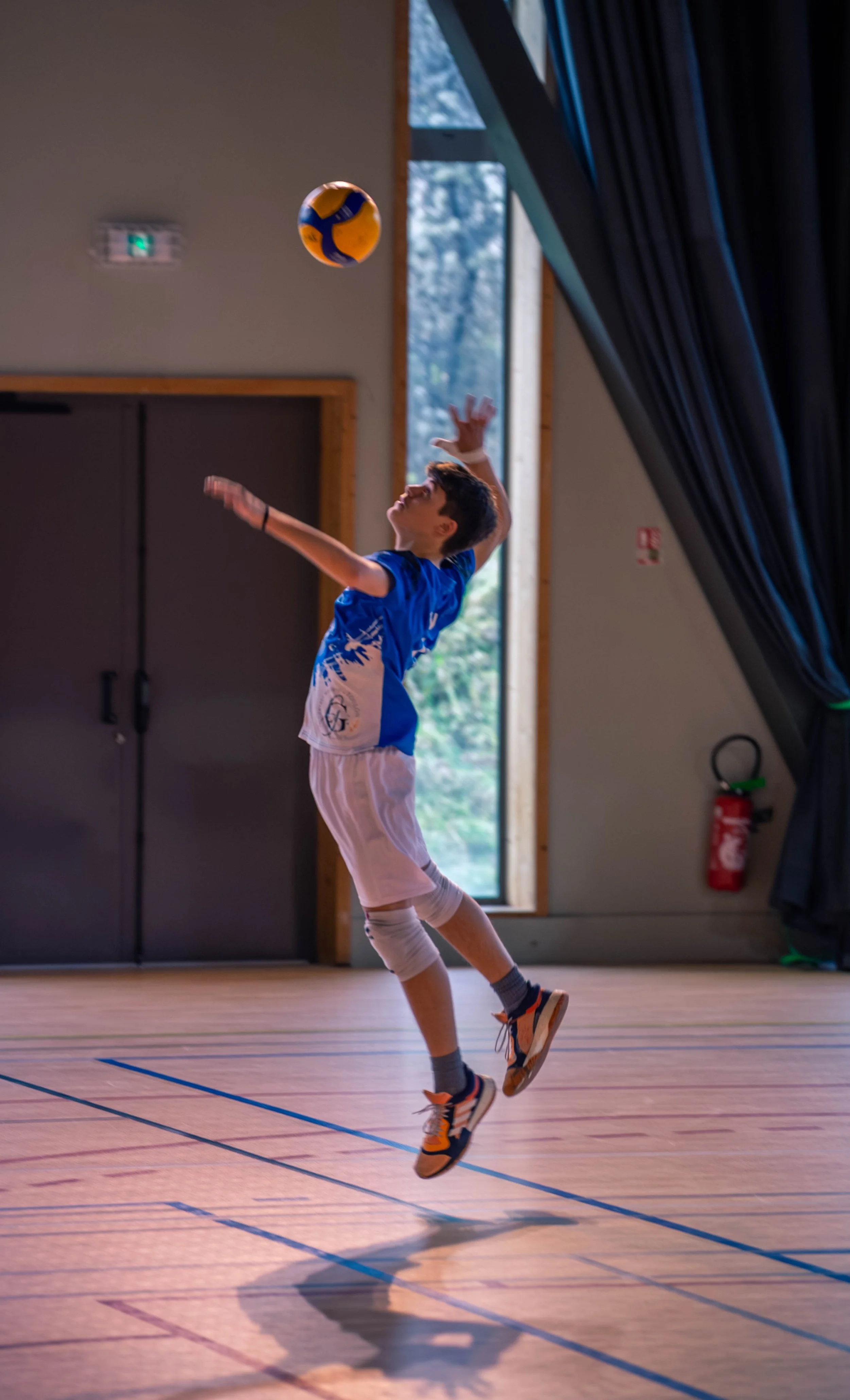 Un garçon en vêtements de sport joue au volley-ball dans une salle de sport intérieure, sautant pour frapper le ballon.