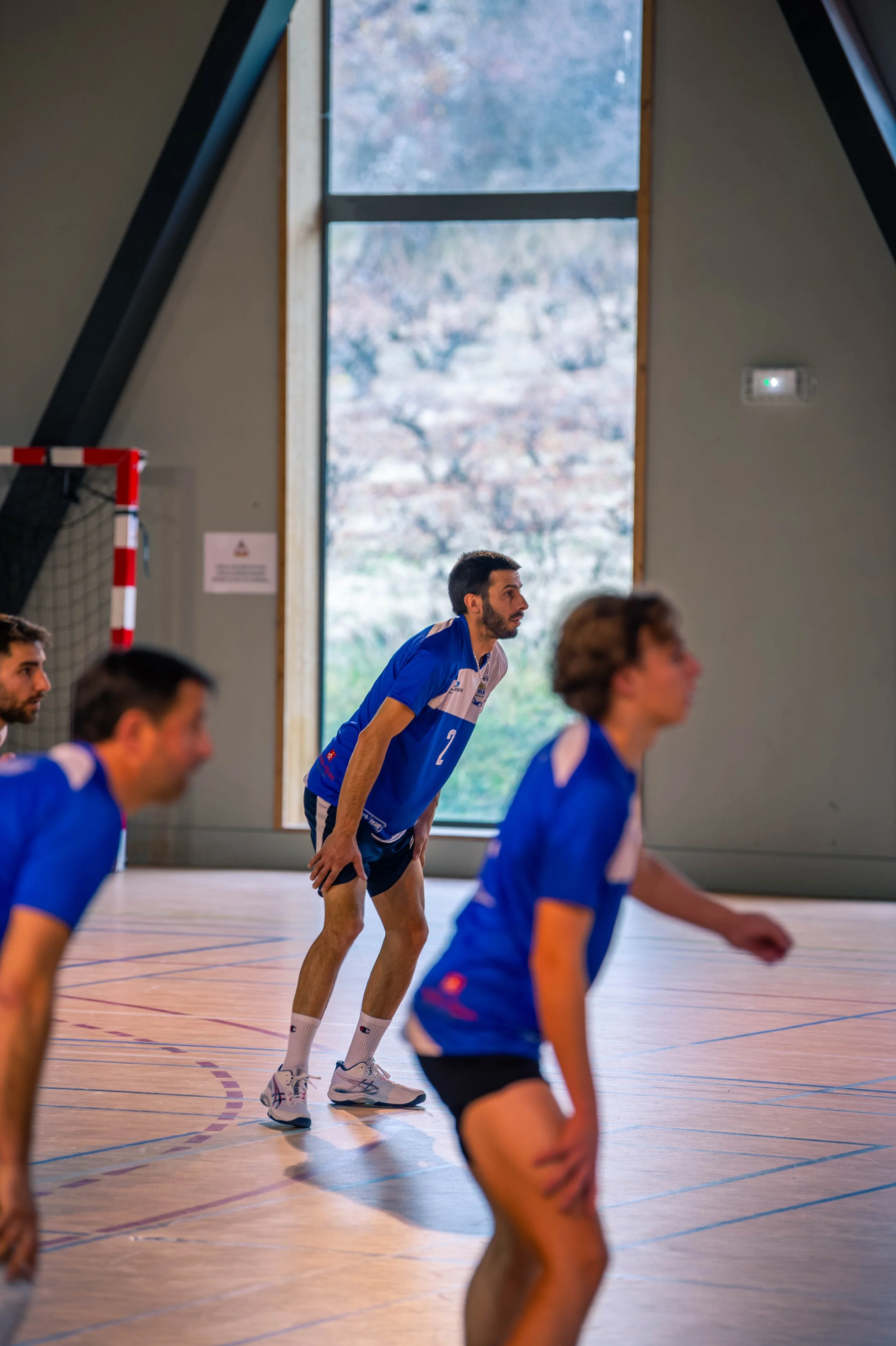 Des joueurs de volleyball s'entraînent dans une salle intérieure avec une grande fenêtre laissant entrer la lumière naturelle.