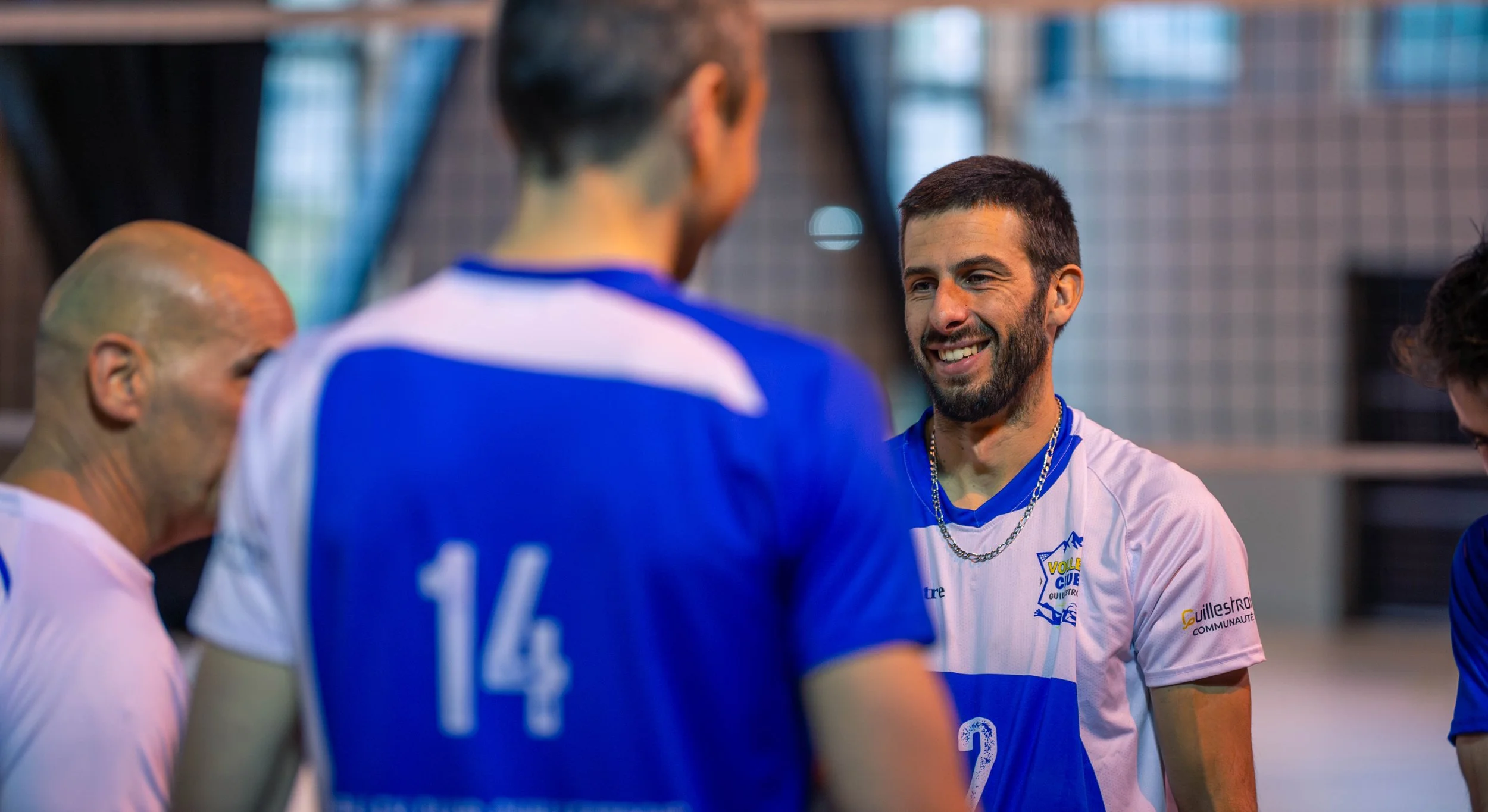 Groupe de joueurs de volley-ball discutant et souriant lors d'un match ou entraînement dans un gymnase.