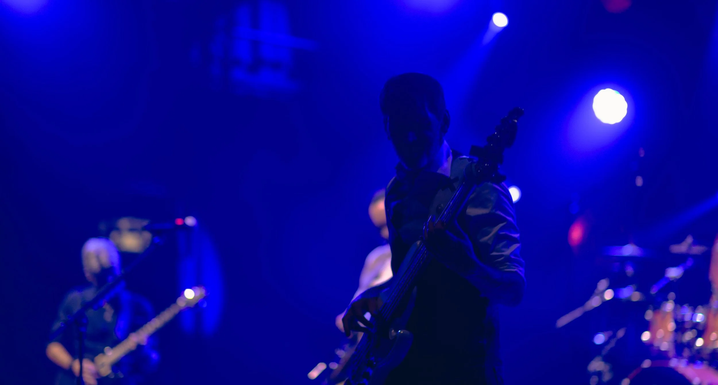 Musiciens en concert sous éclairage bleu, un guitariste au centre tenant une guitare électrique.