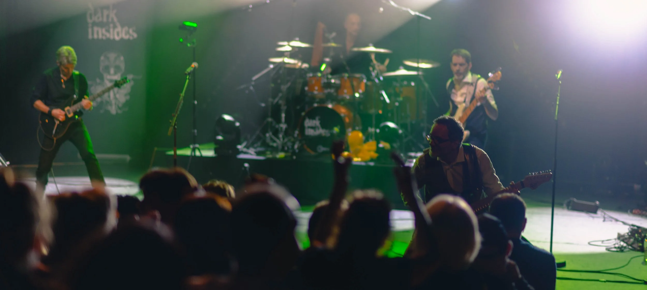 Un groupe de musiciens en performance en concert, avec une scène illuminée en vert et un public en premier plan.