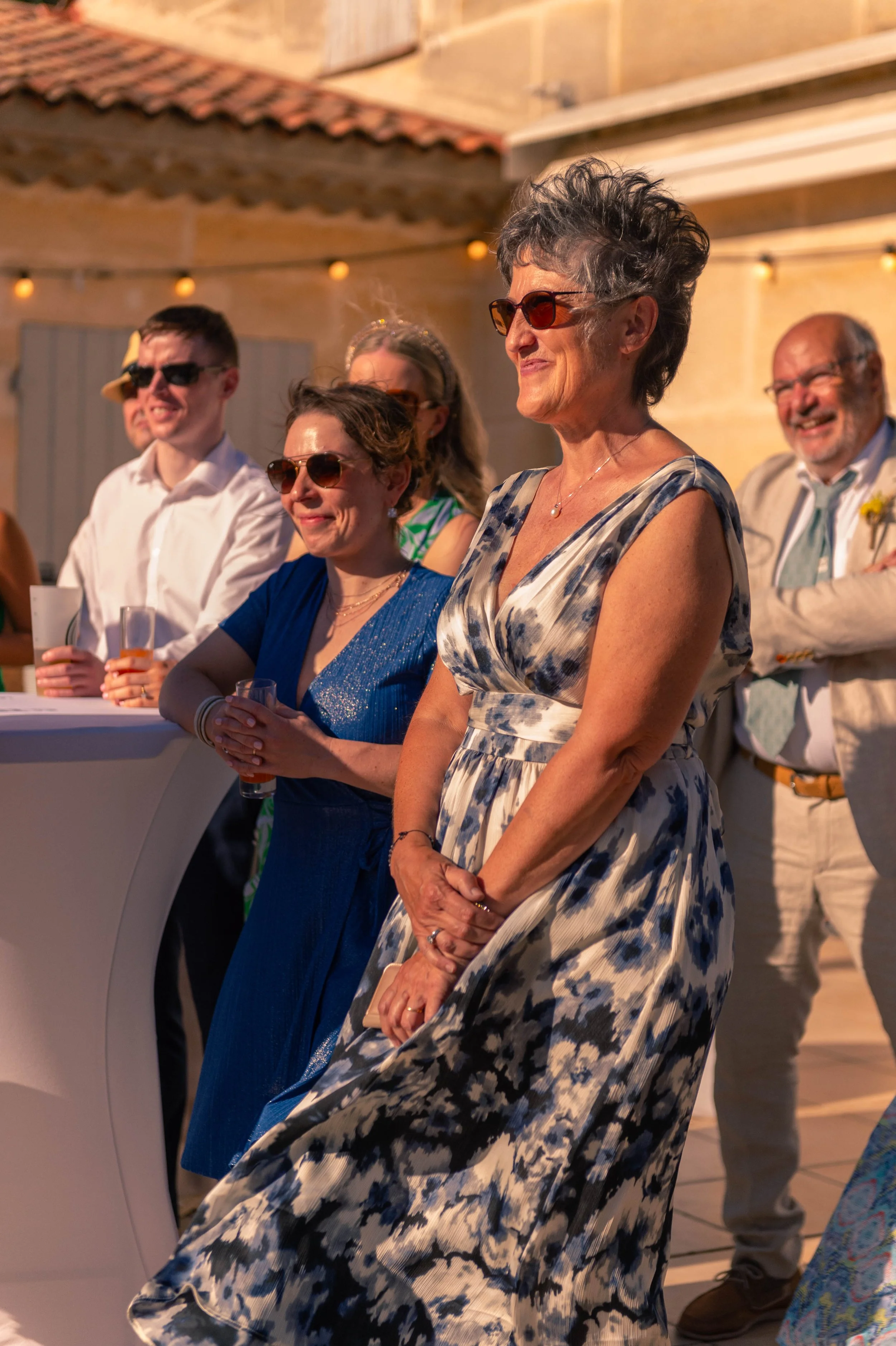 Groupe de personnes élégamment habillées, portant des lunettes de soleil, lors d'une réception ou fête en intérieur ou en terrasse avec décor lumineux.