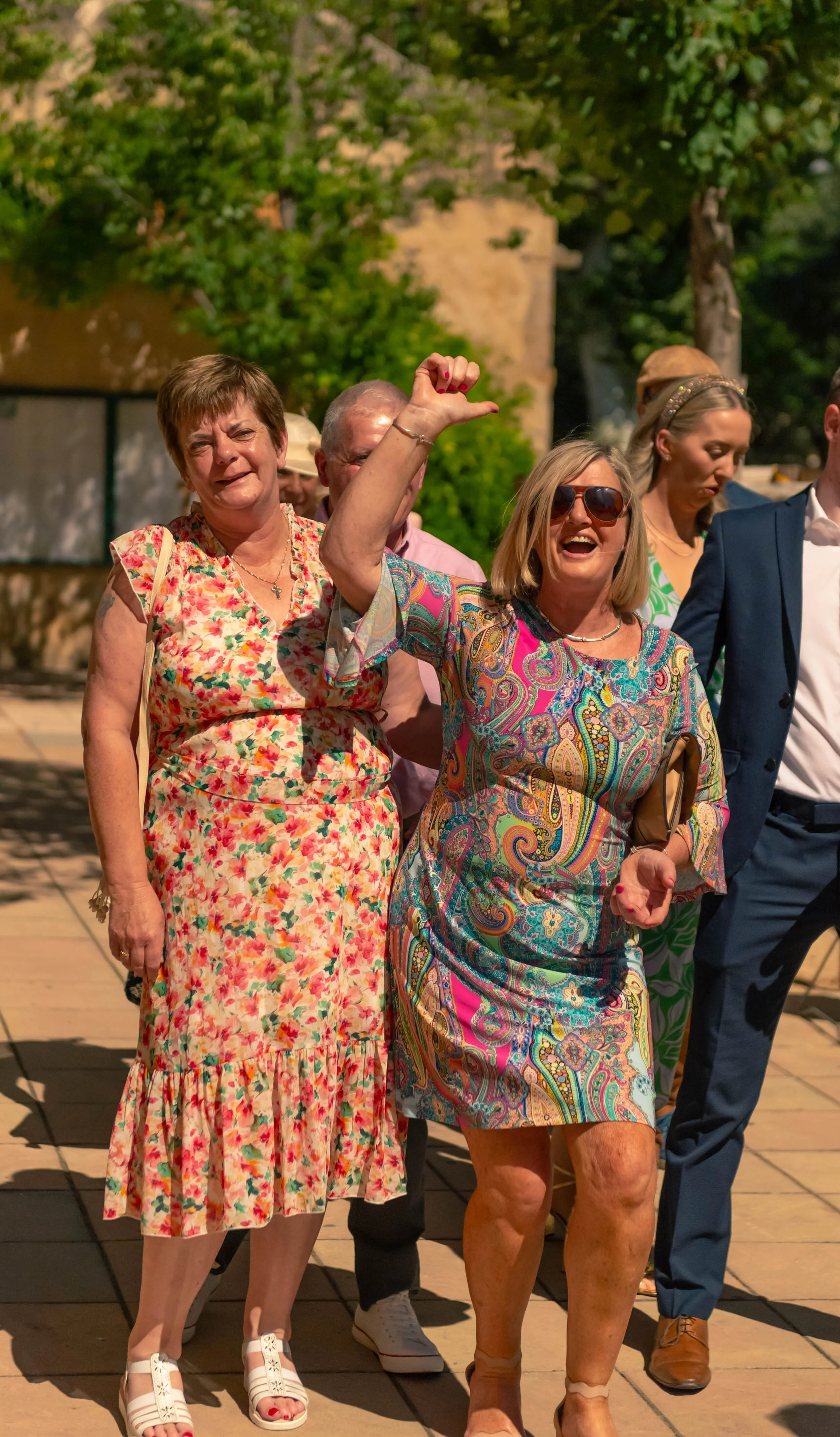 Groupe de personnes souriantes et en tenue estivale lors d'une sortie en plein air, avec un fond de végétation et un bâtiment ancien.