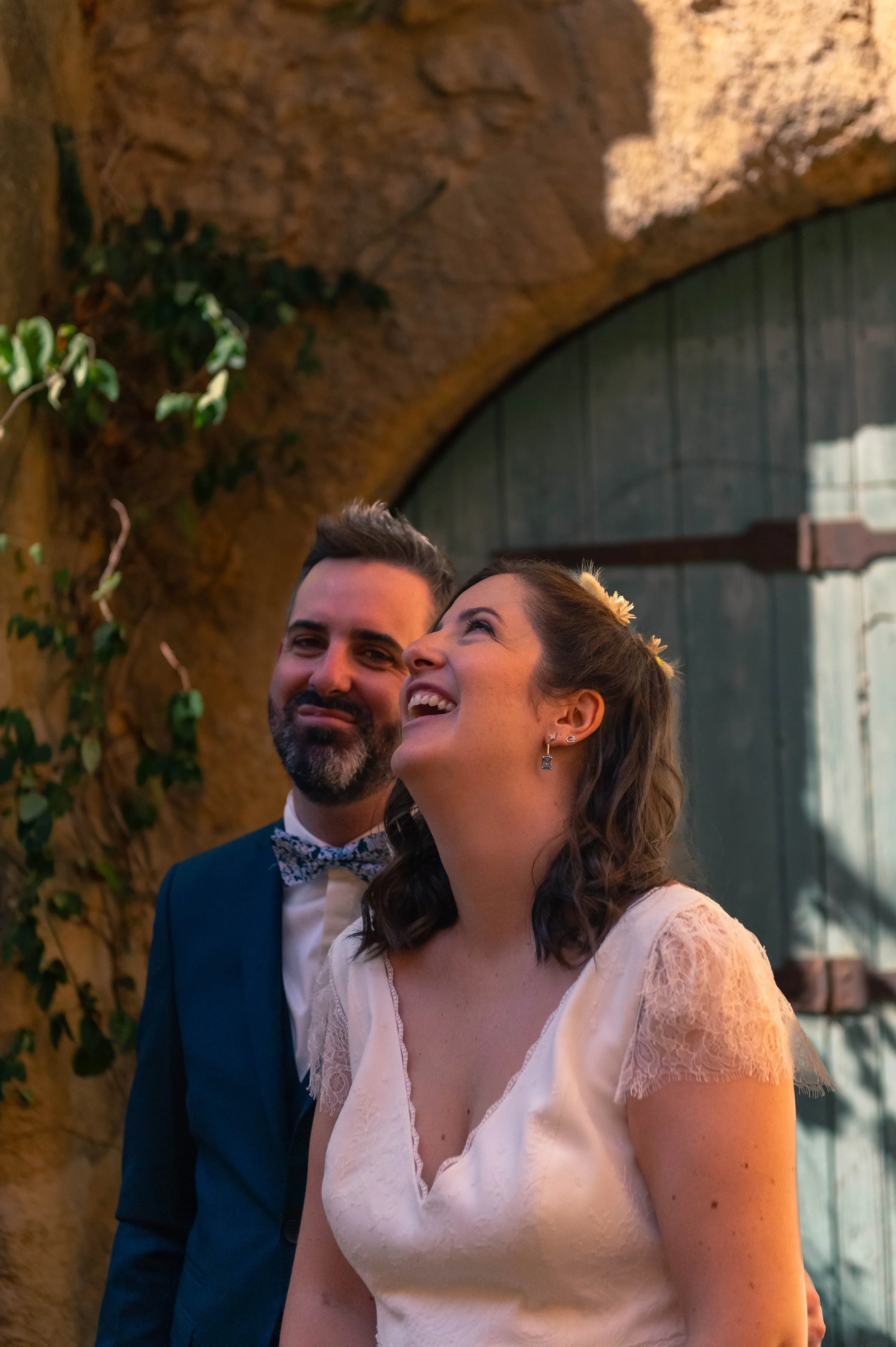 Un couple souriant lors d'une cérémonie ou d'un mariage, à l'intérieur avec un mur en pierre et une grande porte en bois