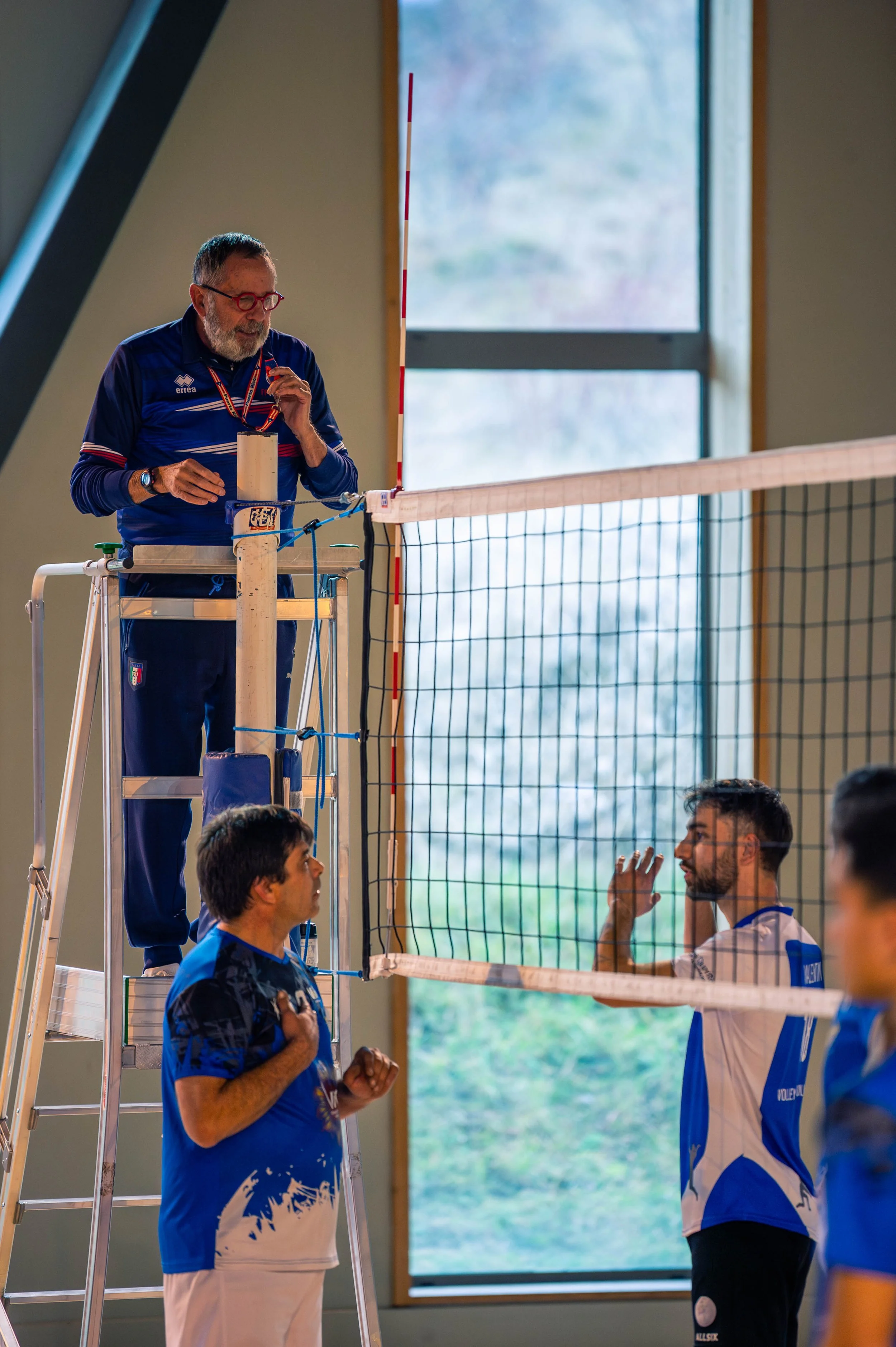 Une équipe de volleyball en train de s'entraîner ou de jouer, avec un officiel en haut d'une plateforme qui donne des instructions ou une consigne.
