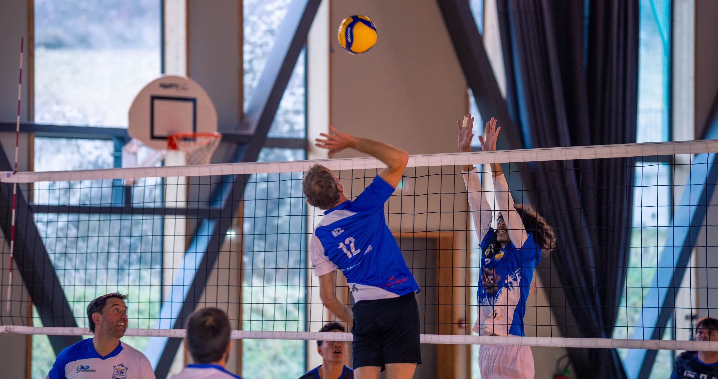 Deux joueurs de volley-ball, l'un en bleu et l'autre en blanc, sautent pour un contre à un filet lors d'un match intérieur.