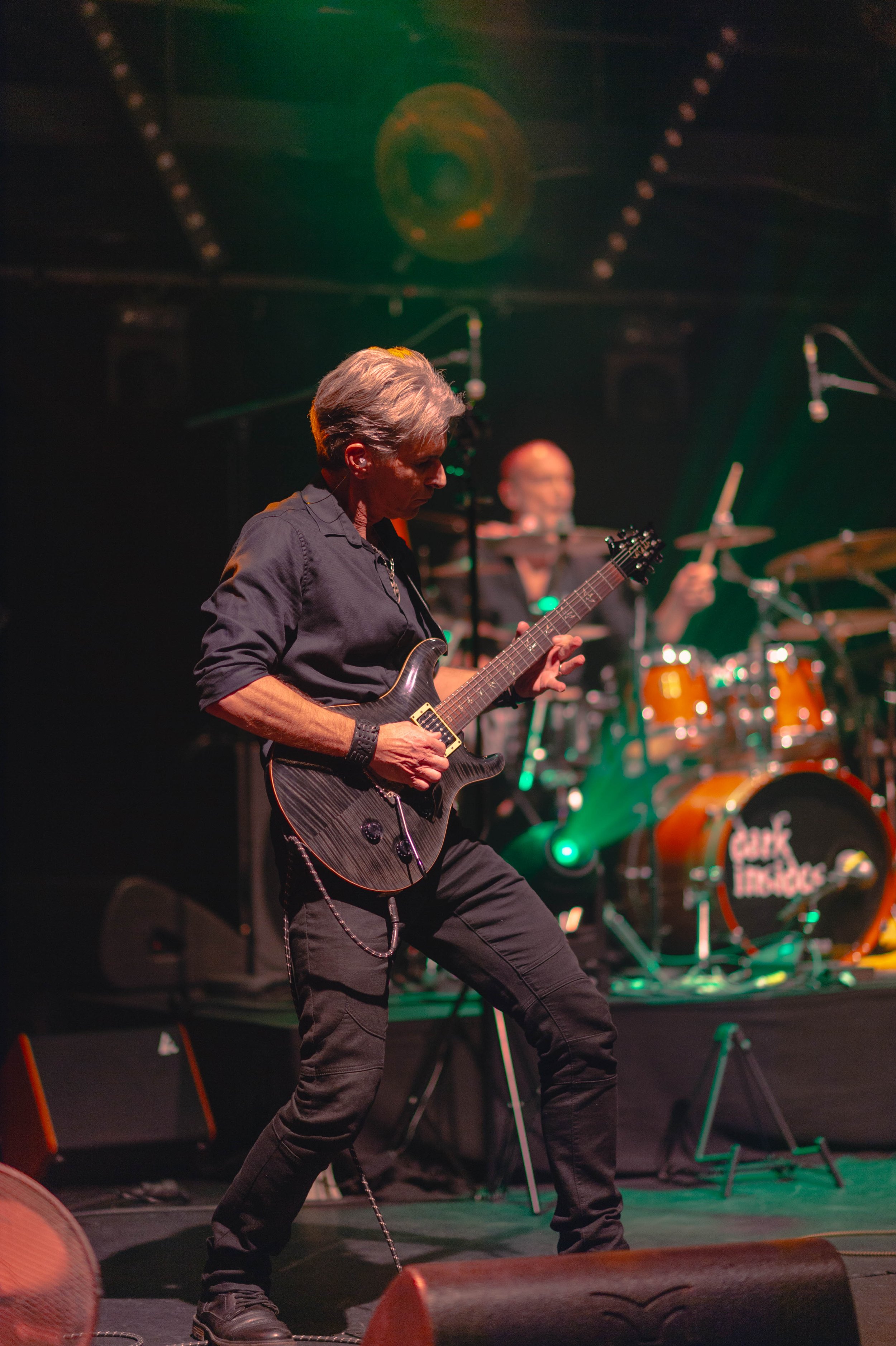 Un musicien jouant de la guitare électrique en concert avec un groupe en arrière-plan sur scène.