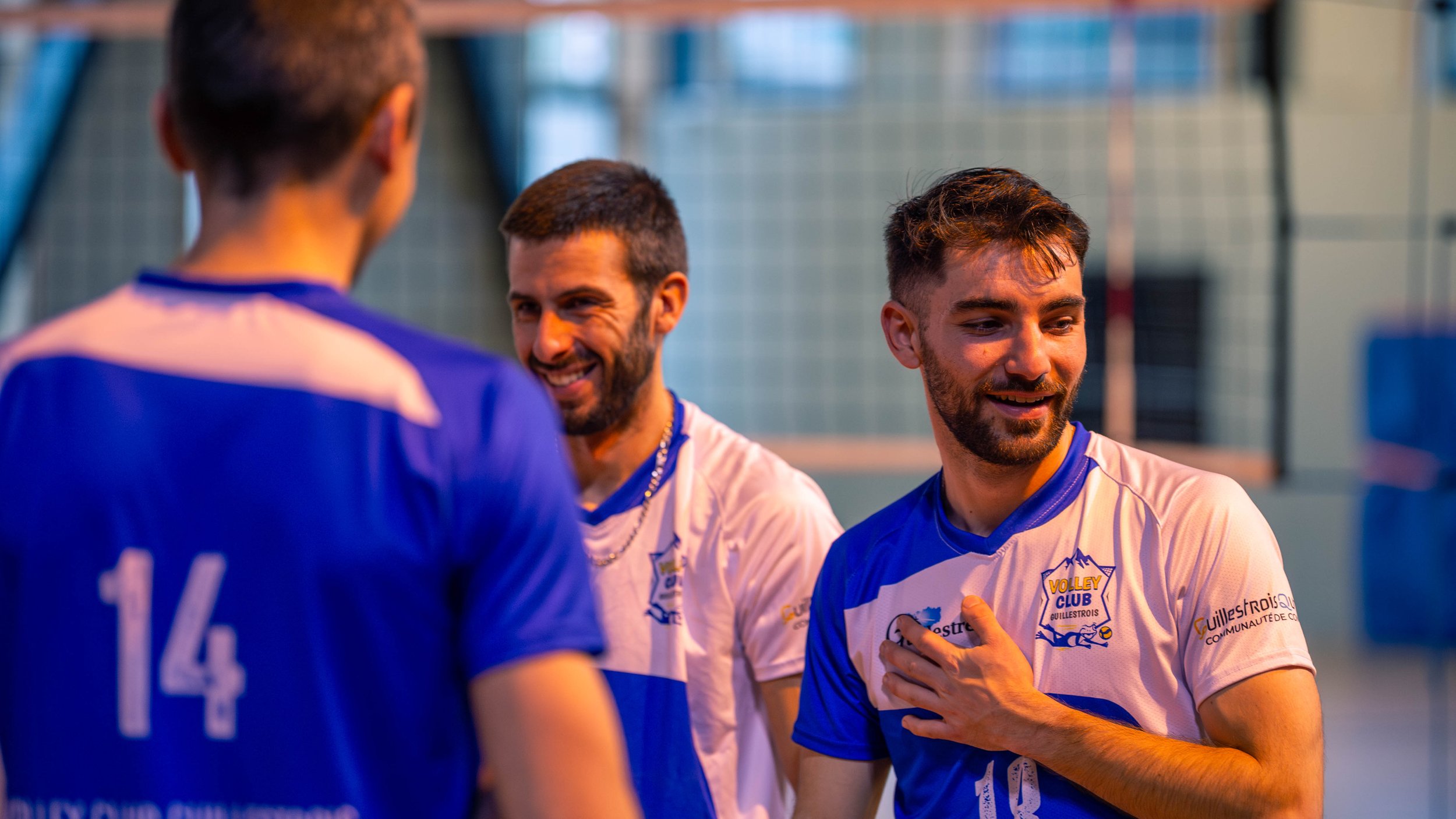 Trois joueurs de volley-ball en tenue sportive discutent sur un court intérieur.