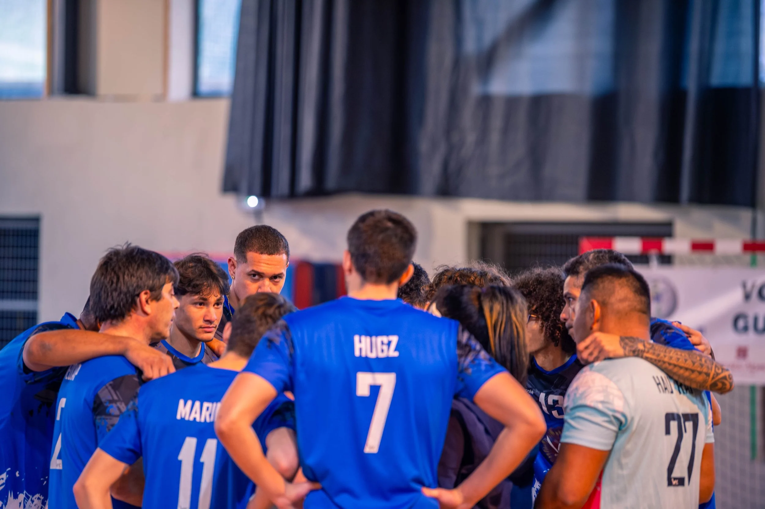 Groupe de joueurs de volleyball en cercle pendant un temps d'encouragement, certains avec les bras sur les épaules.