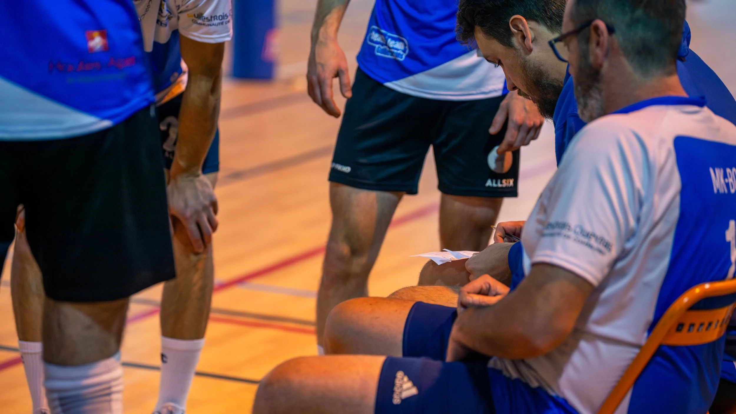 Joueurs de volleyball en réunion d'équipe sur un terrain en bois.