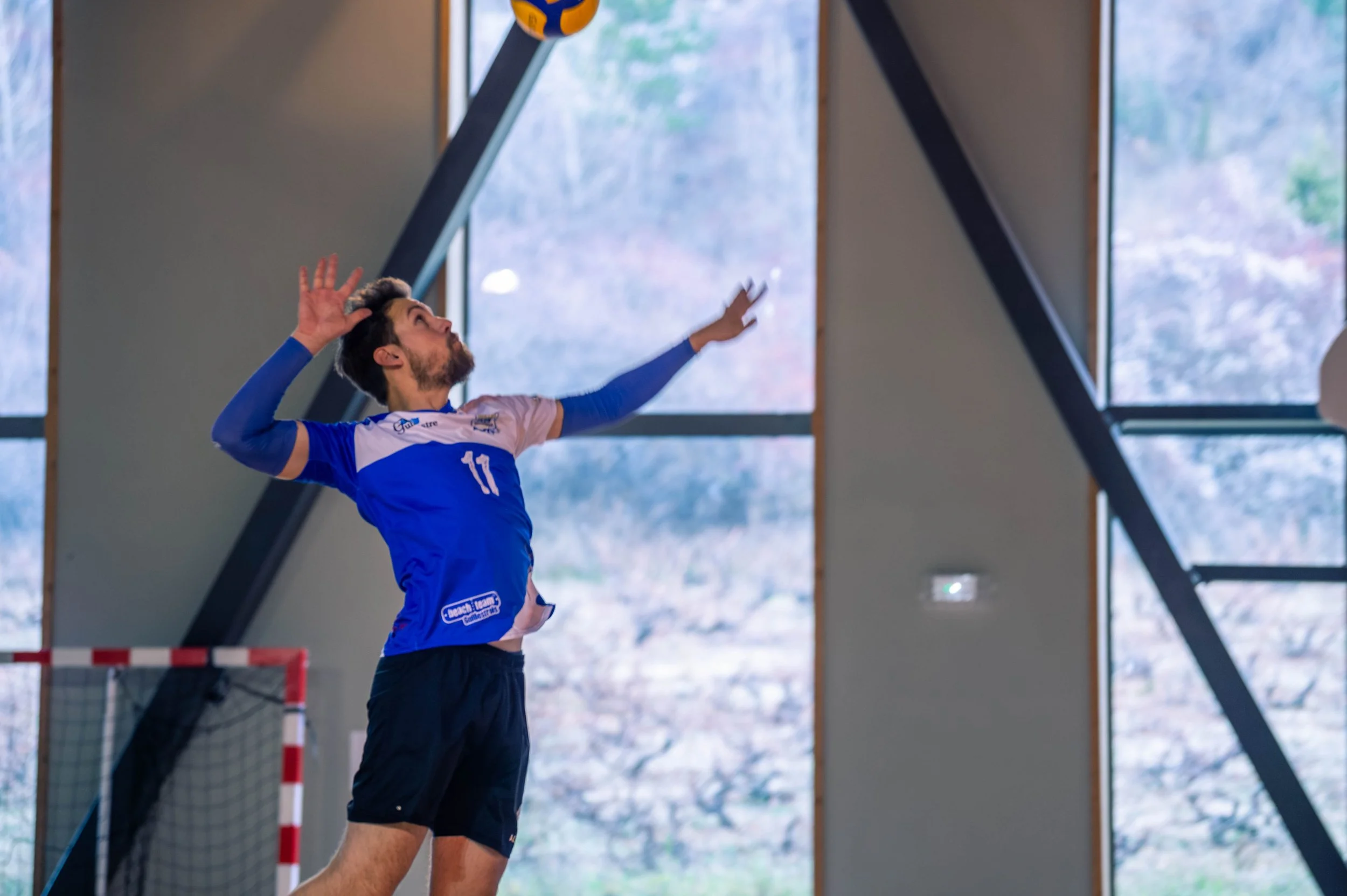 Un joueur de volley-ball en train de sauter pour frapper le ballon dans une salle intérieure.