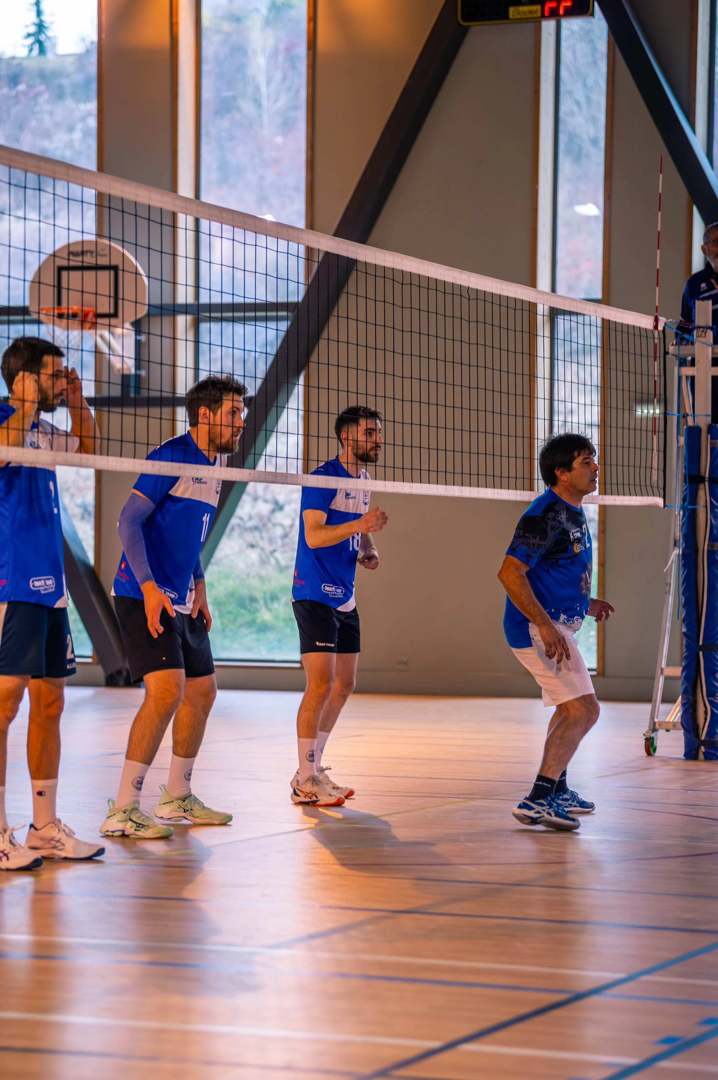 Joueurs de volleyball en tenue bleue se tenant en ligne dans un gymnase, prêts à commencer un match.