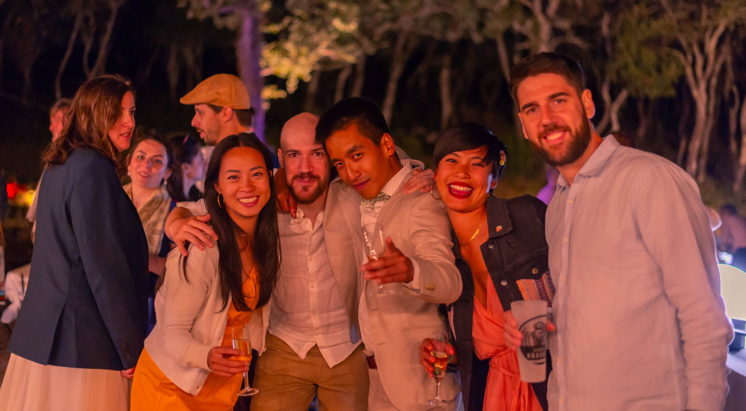 Groupe de personnes souriantes lors d'une fête en extérieur la nuit, tenant des verres, posant pour la photo.
