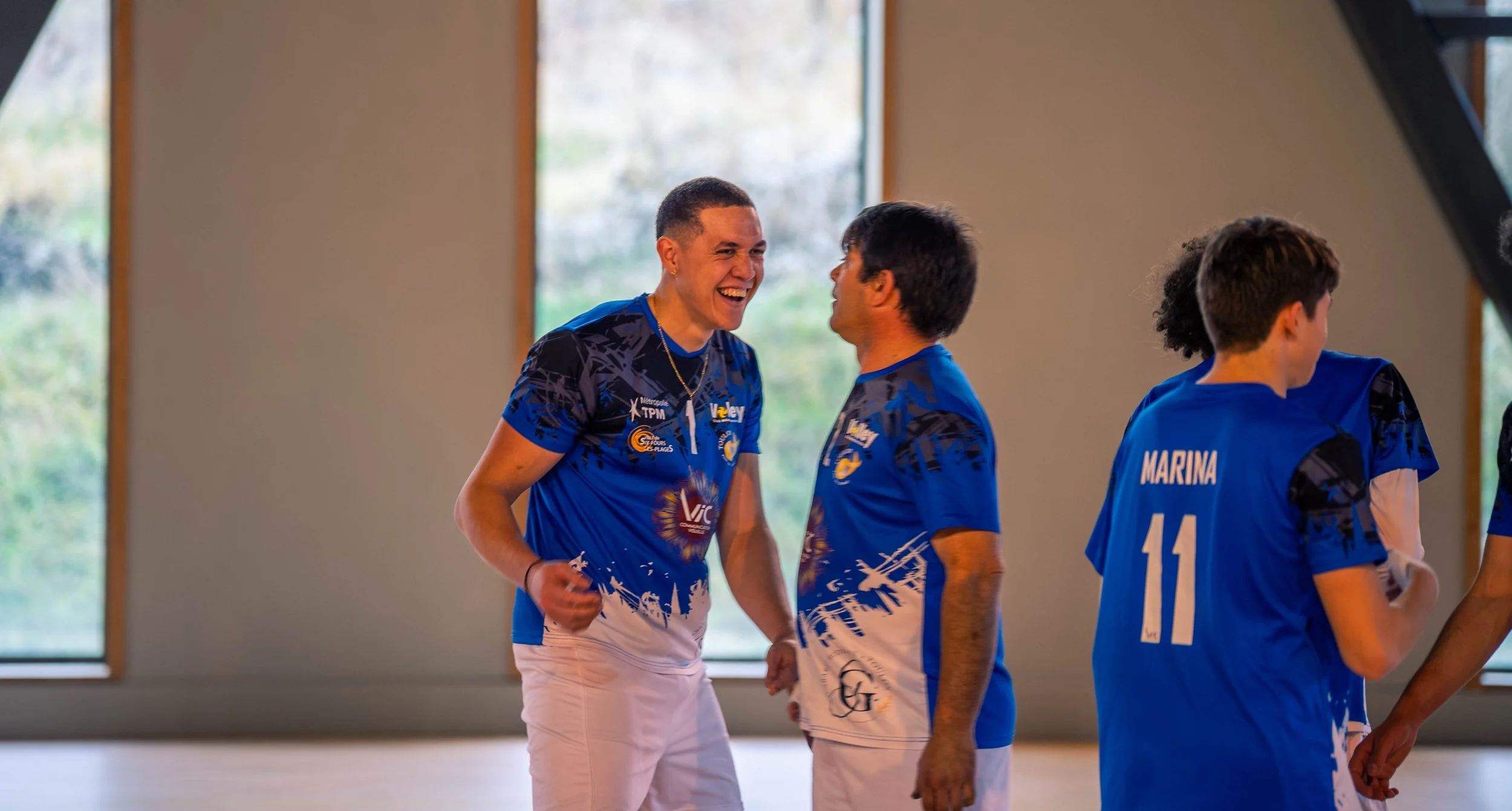 Groupe de jeunes athlètes en tenue de sport bleue, partageant un moment de joie et de camaraderie dans un gymnase.