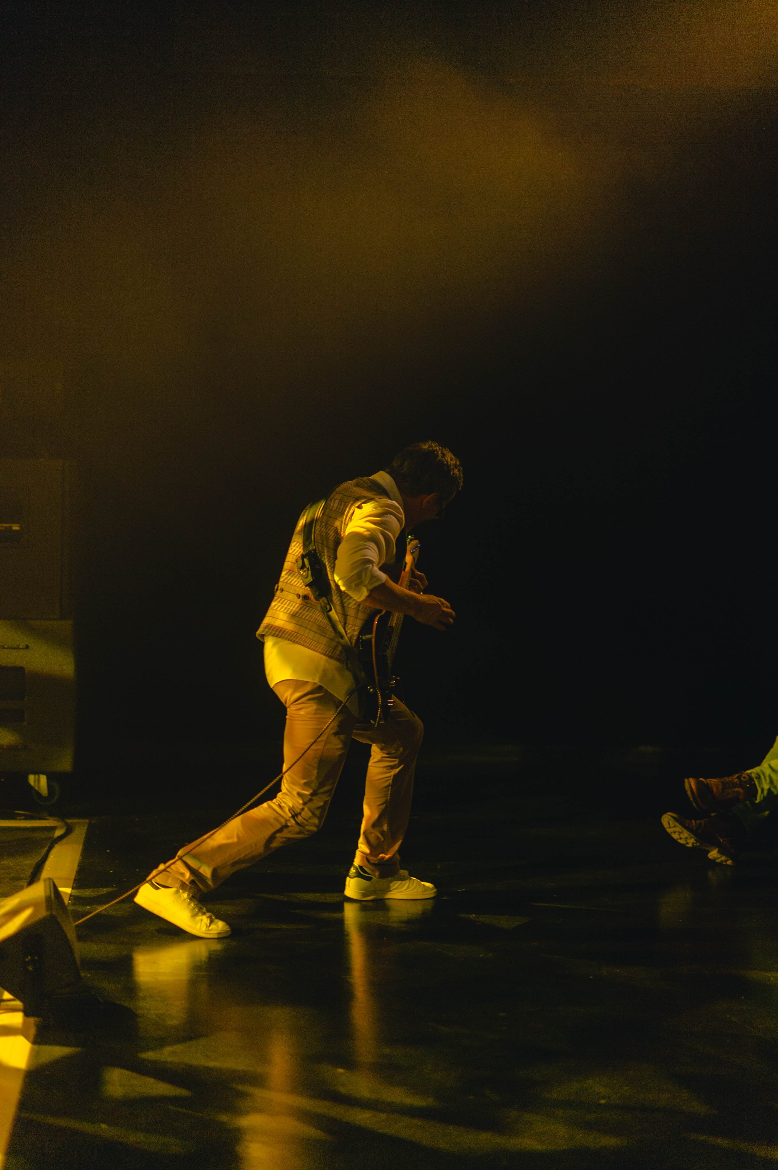 Un homme joue de la guitare sur scène, éclairé par un éclairage jaune, en position de jam ou de performance musicale.