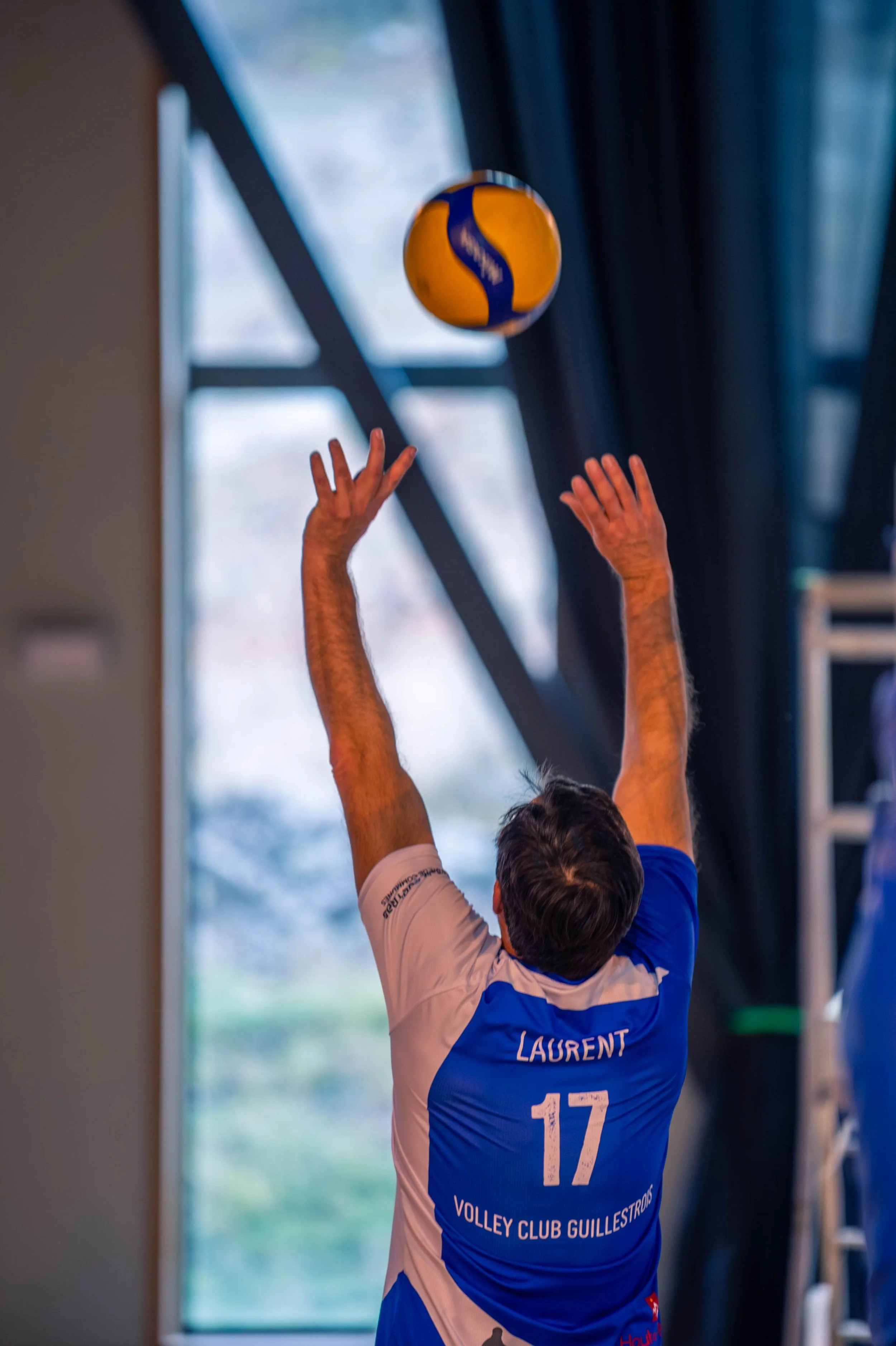 Un joueur de volley-ball, portant un maillot avec le nom Laurent et le numéro 17, effectue un saut pour tenter un coup lors d'un match intérieur.