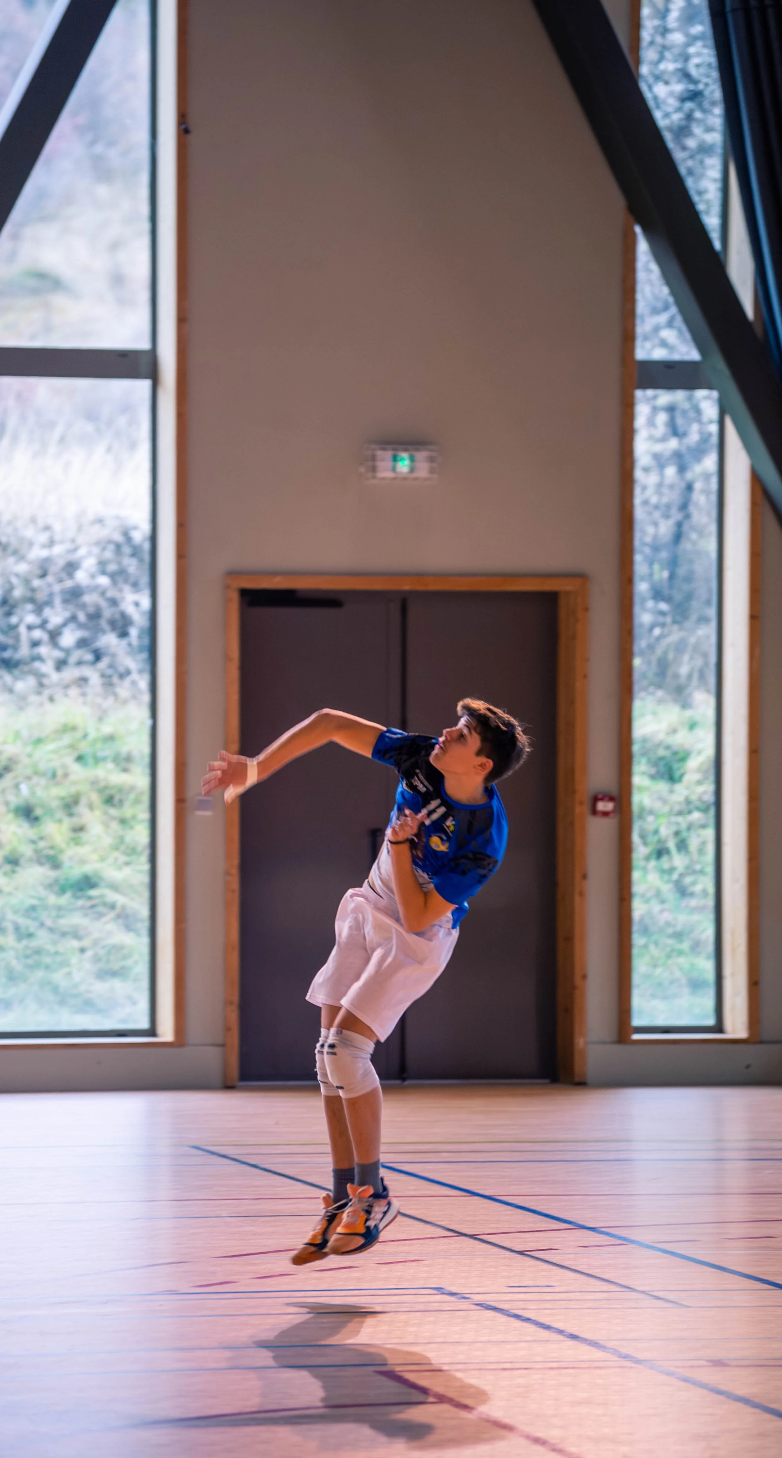 Un jeune homme en tenue de sport joue au tennis en intérieur, sautant dans les airs avec une raquette à la main.