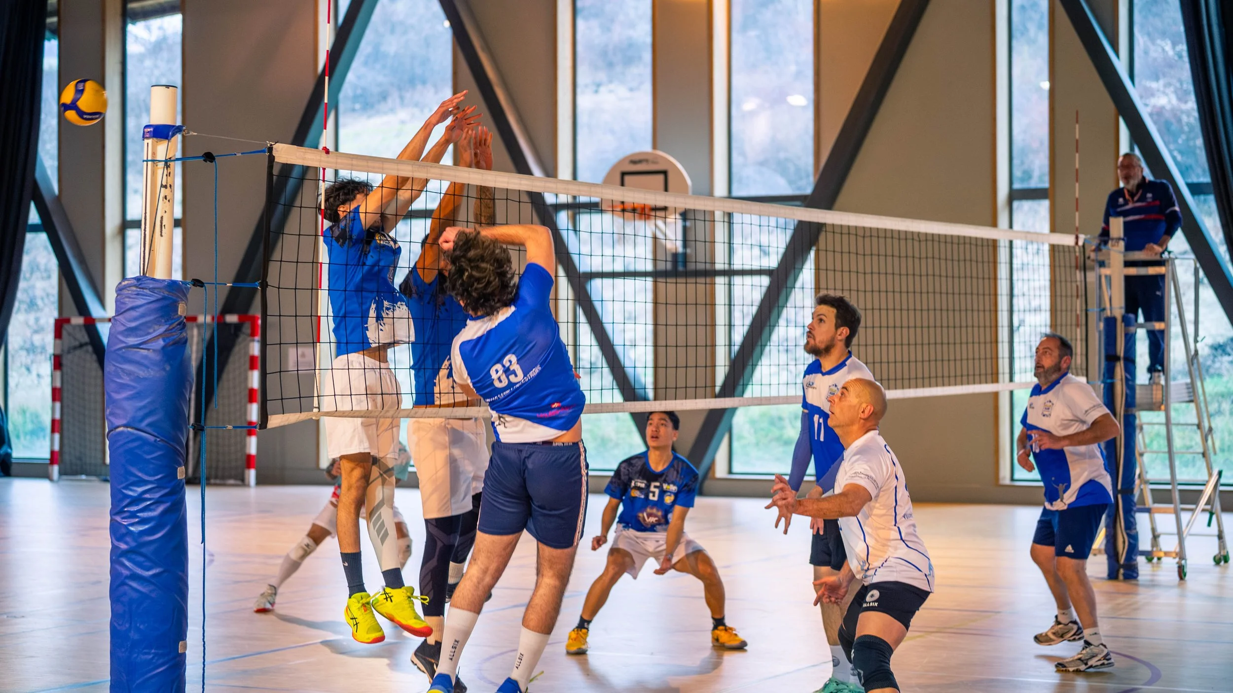 Une partie de volleyball en salle avec des joueurs en action, certains sautant pour attaquer ou bloquer, d'autres préparant une réception