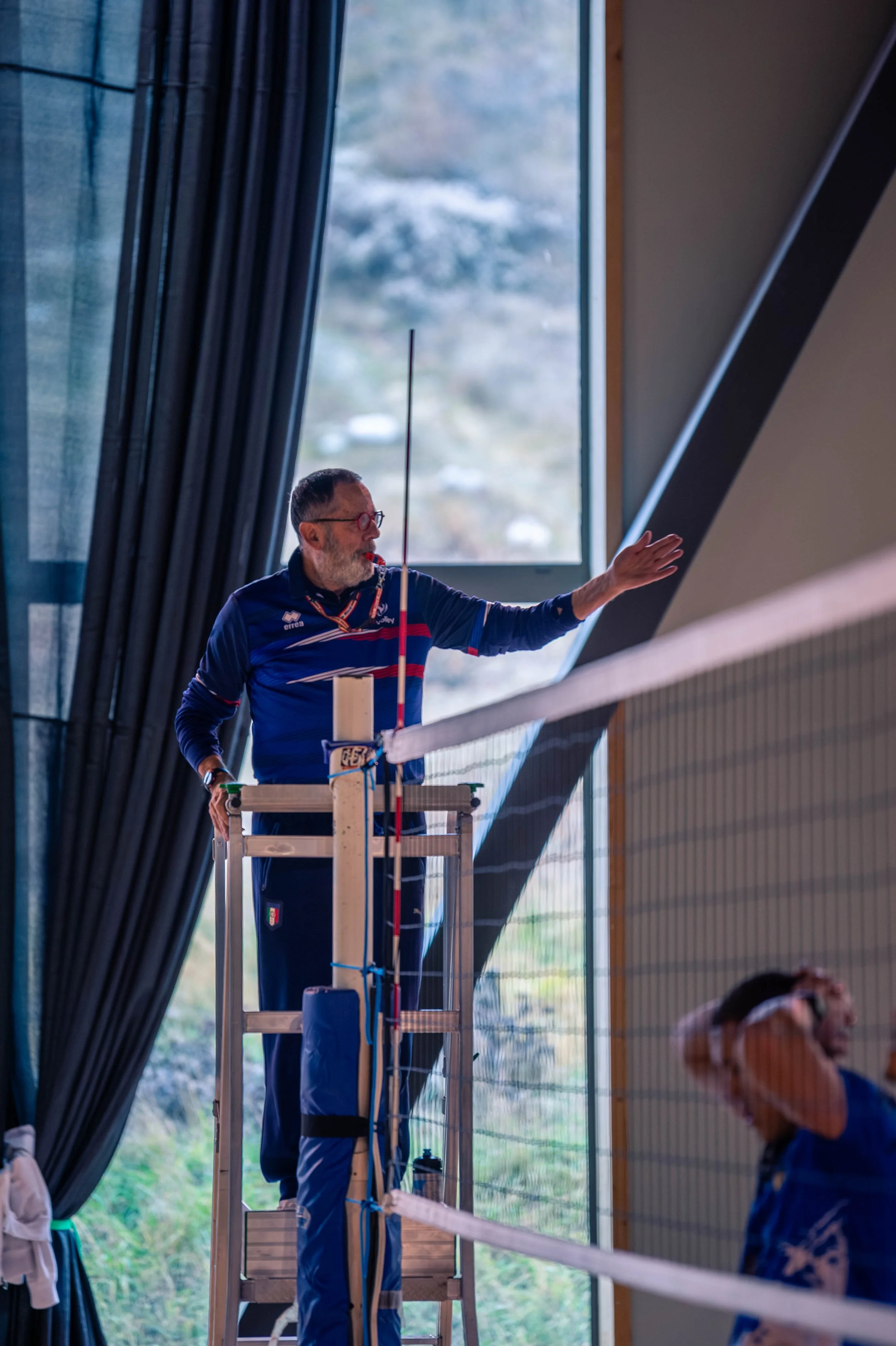 Un arbitre derrière le filet lors d'un match de volleyball intérieur, faisant une gesture avec la main.