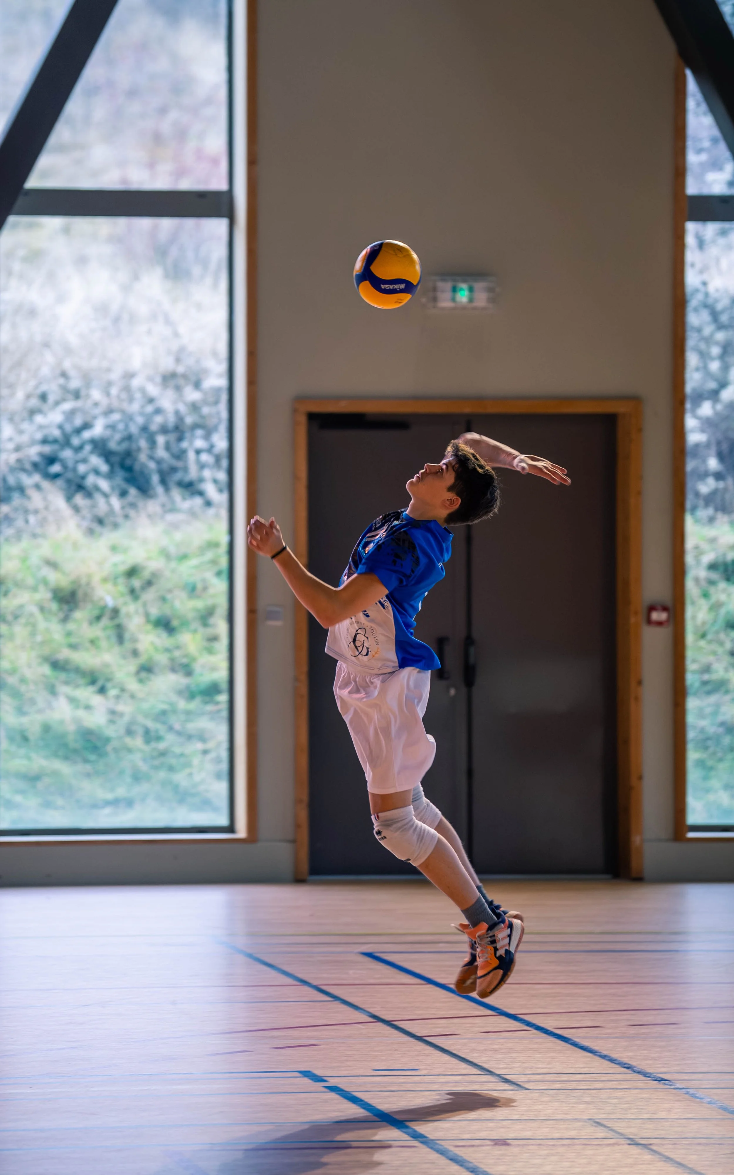 Un garçon en tenue de volley-ball saute dans un gymnase pour frapper un ballon de volley en l'air.