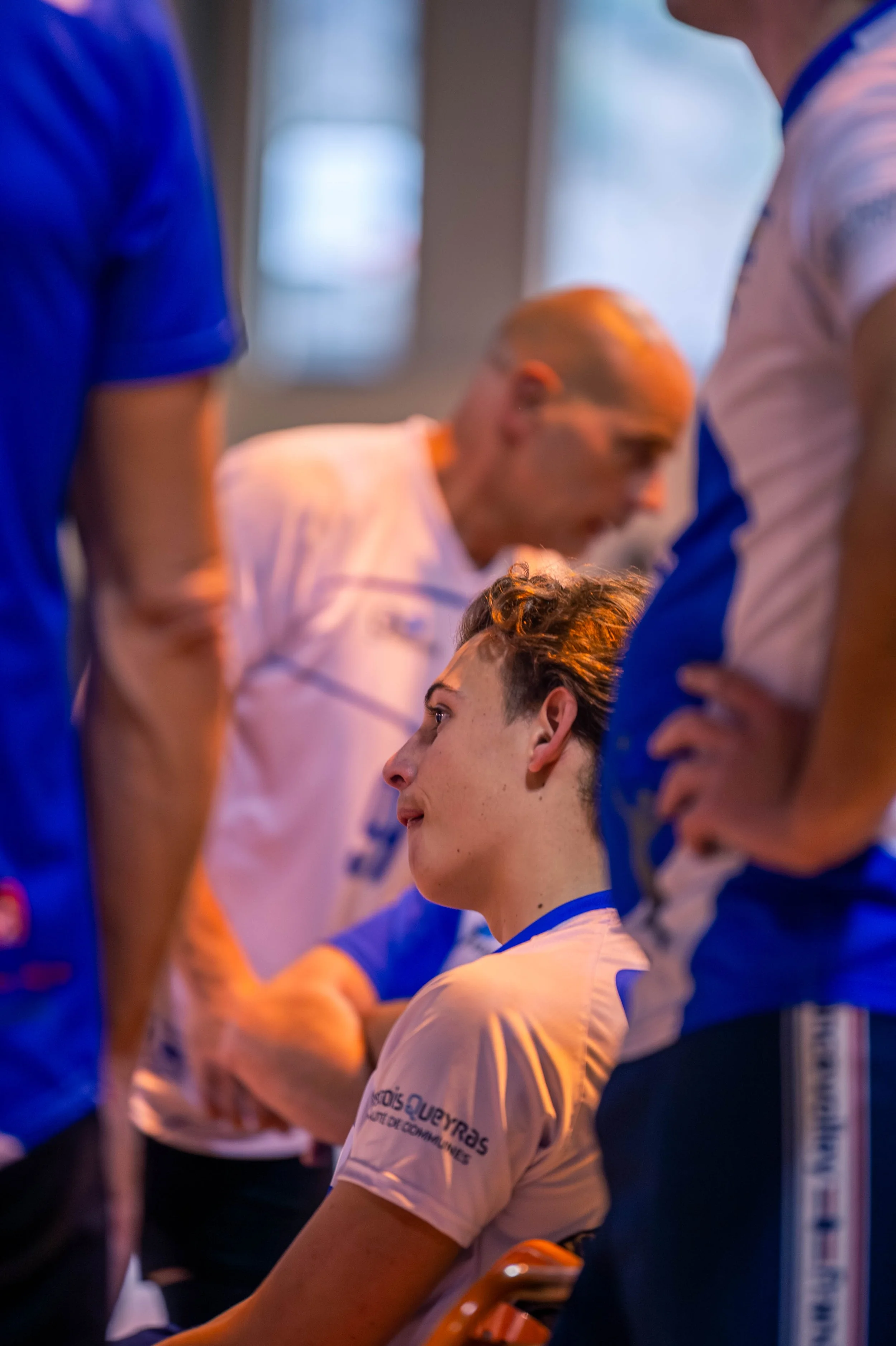 Une équipe sportive en train de discuter, avec une jeune femme assise au centre en train d'écouter attentivement ses coéquipiers.