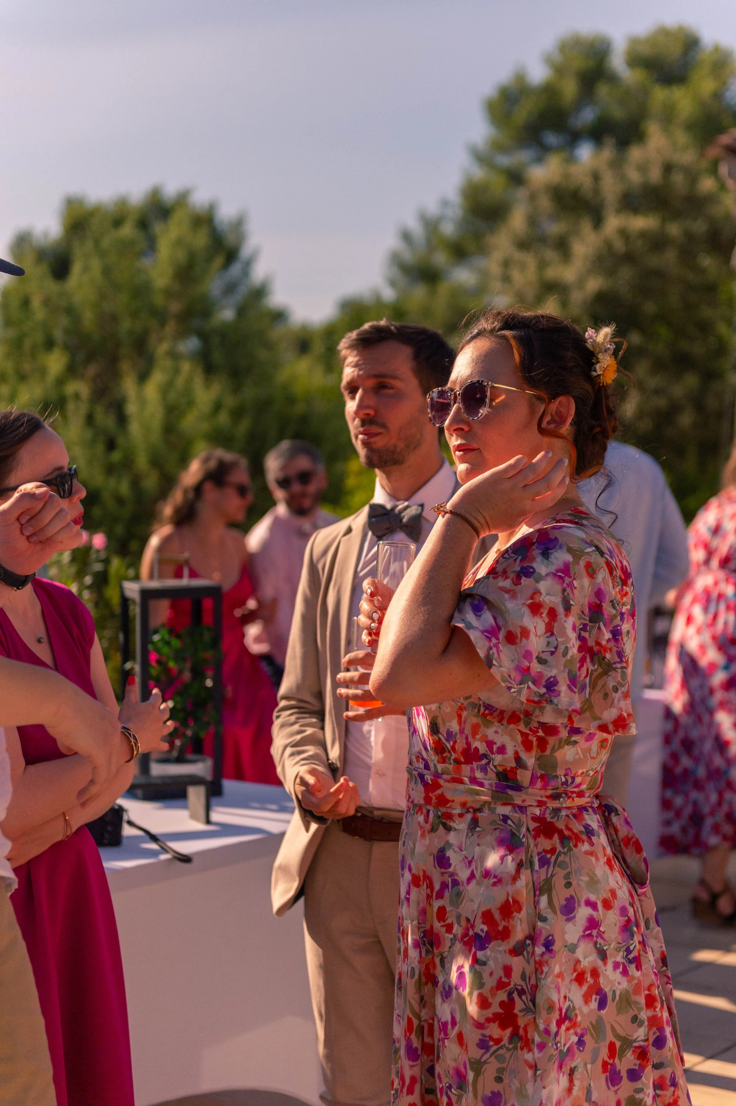 Groupe de personnes lors d'une fête en plein air, portant des vêtements colorés, avec un décor naturel et un ciel ensoleillé.