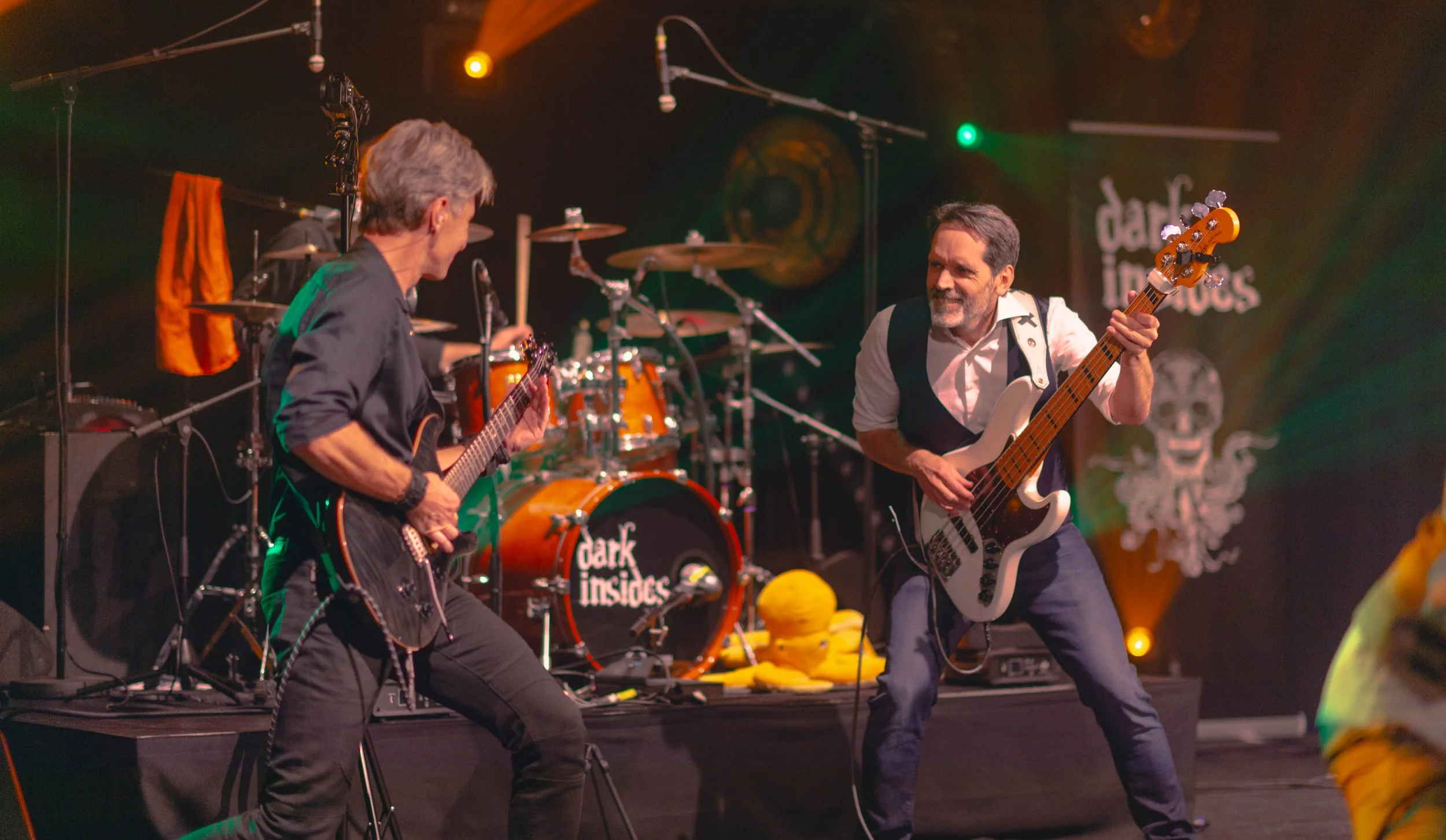 Deux musiciens jouent de la musique sur scène, une guitare électrique et une basse, avec un fond de logo 'dark insides'