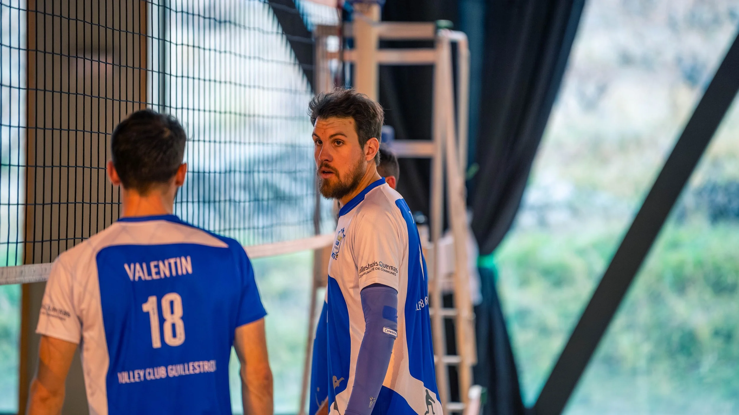 Deux joueurs de volley-ball en conversation, portant des maillots bleus et blancs, dans une salle d'arcade