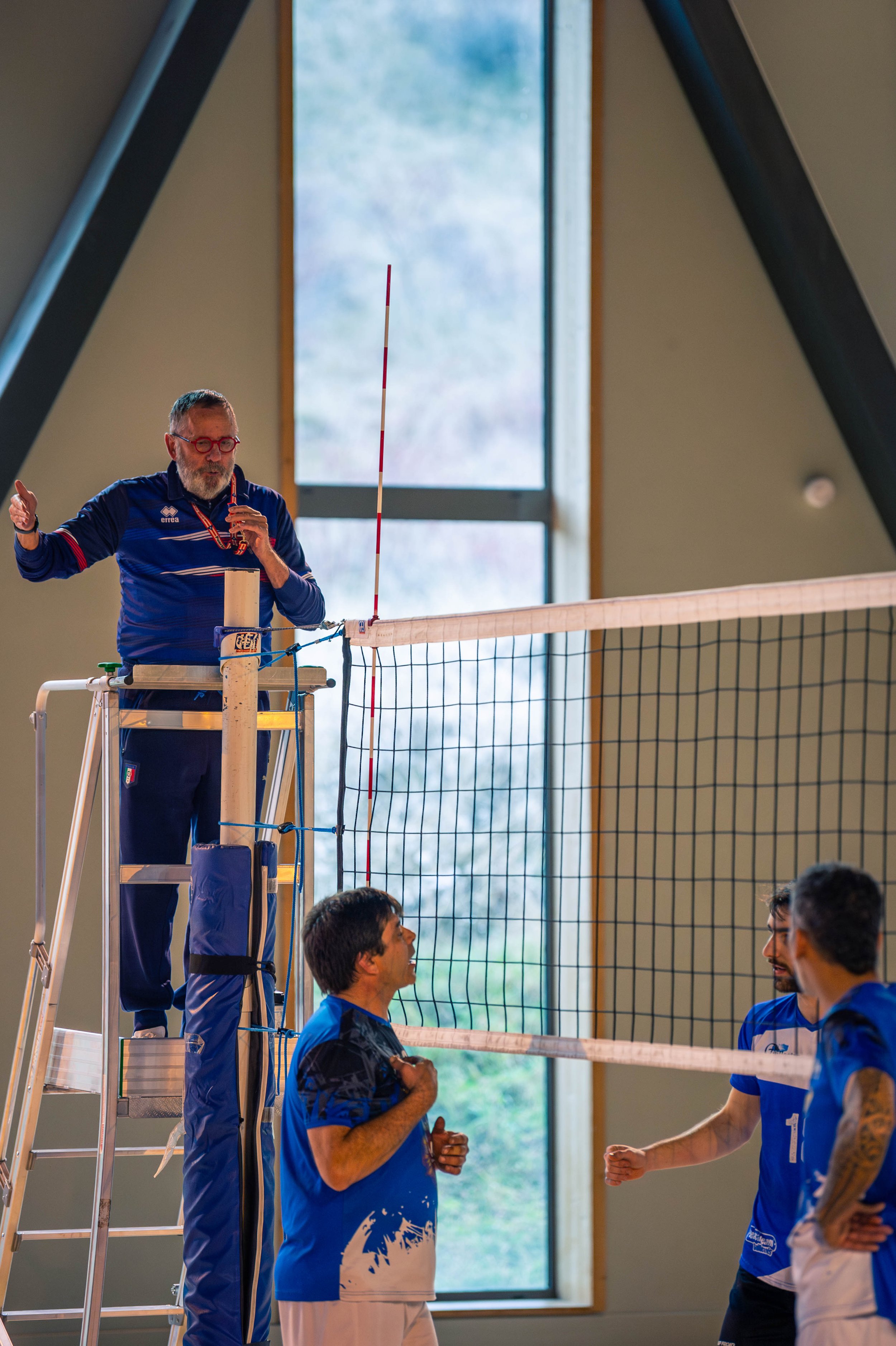 Arbitre de volleyball en haut de la plateforme s'adressant à des joueurs lors d'un match intérieur.