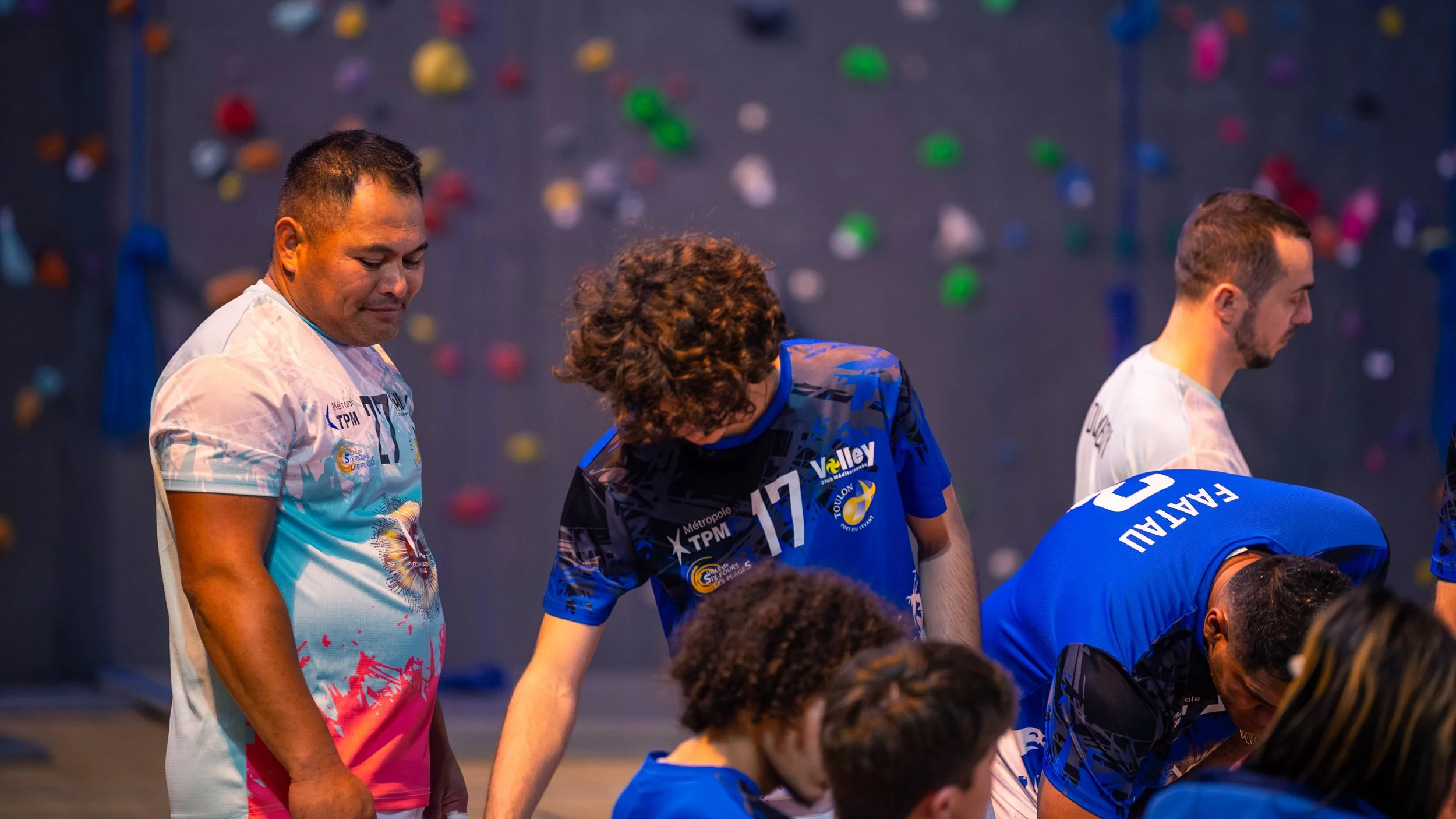 Des joueurs de volleyball s'encourageant lors d'une pause de match dans une salle avec un mur d'escalade en arrière-plan.