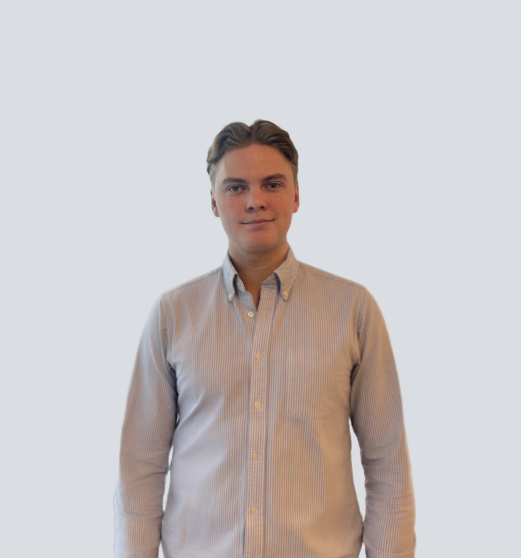 Young man with brown hair wearing a striped button-up shirt, standing against a plain light gray background.