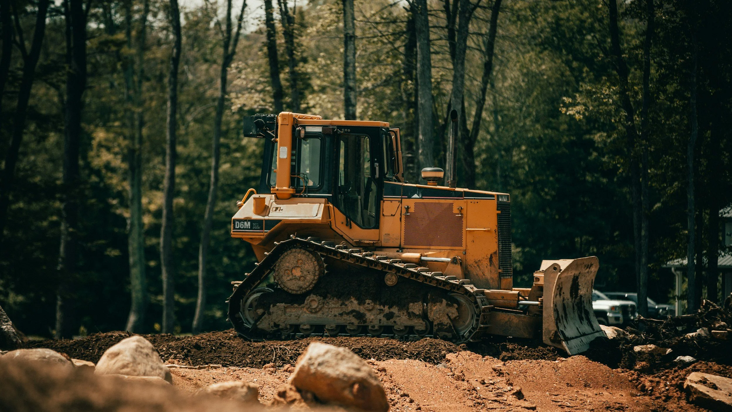 A yellow bulldozer working on a dirt lot in a wooded area.